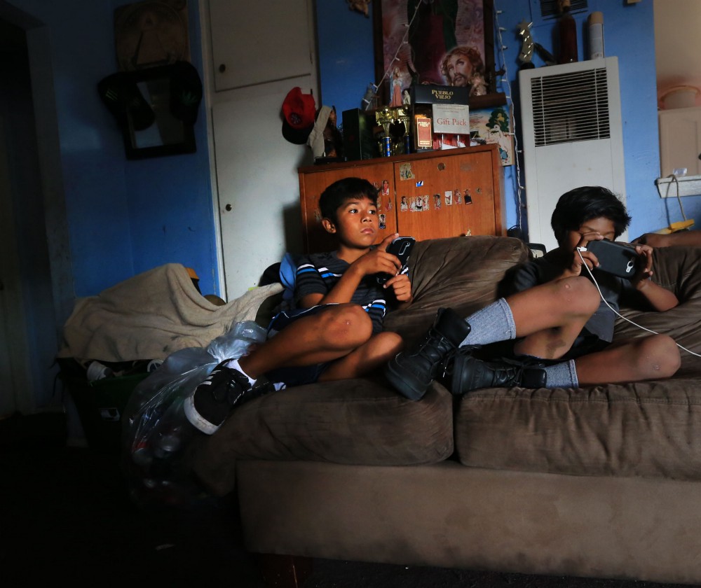 Cesar Gaspar, (left), and his younger brother, Peter, play games on their mobile phones in their apartment living room in Santa Ana, Ca. CREDIT: Daniel A. Anderson for ThinkProgress