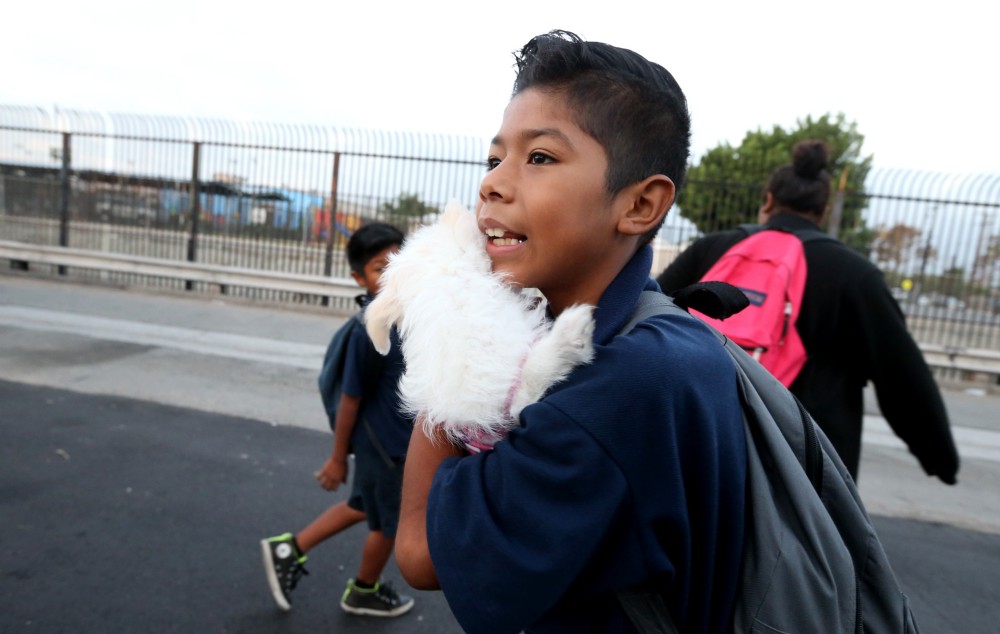 Cesar Gaspar cuddles his family’s pet dog as he walks to school with his younger brother and older sister in Santa Ana, Ca. CREDIT: Daniel A. Anderson for ThinkProgress
