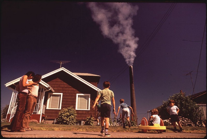 Children play in the yard of a Ruston, Wa. home with a Tacoma smelter stack in the background in 1972. The smelter would have deposited lead, arsenic, and other toxins into the air and surroundings. Photograph by Gene Daniels, US National Archives and Records Administration