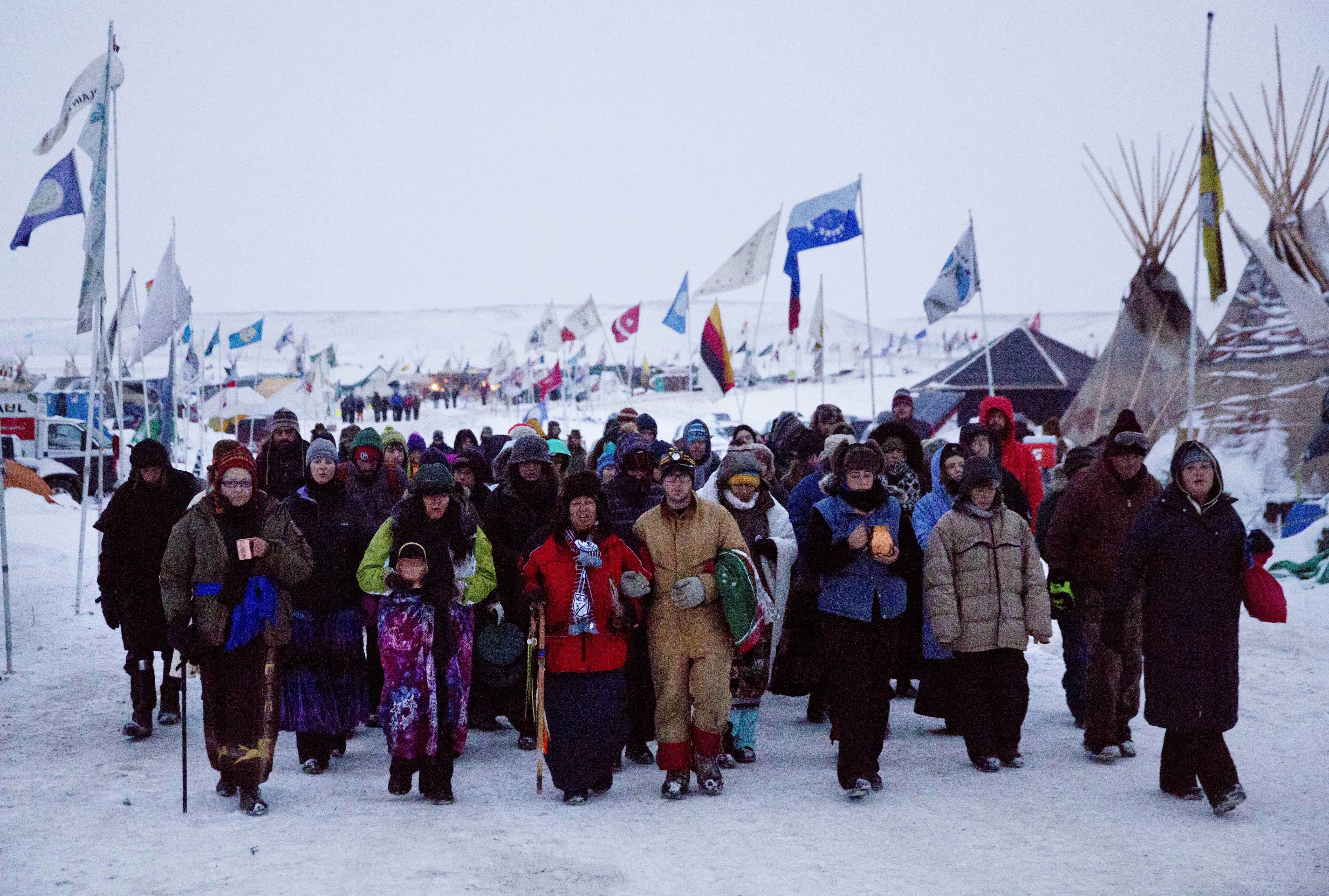 In this December 2016 photo, Beatrice Menase Kwe Jackson, center, walks with Daniel Emory, both of the Ojibwe Native American tribe as they lead a procession to the Cannonball river for a traditional water ceremony. CREDIT: AP Photo/David Goldman