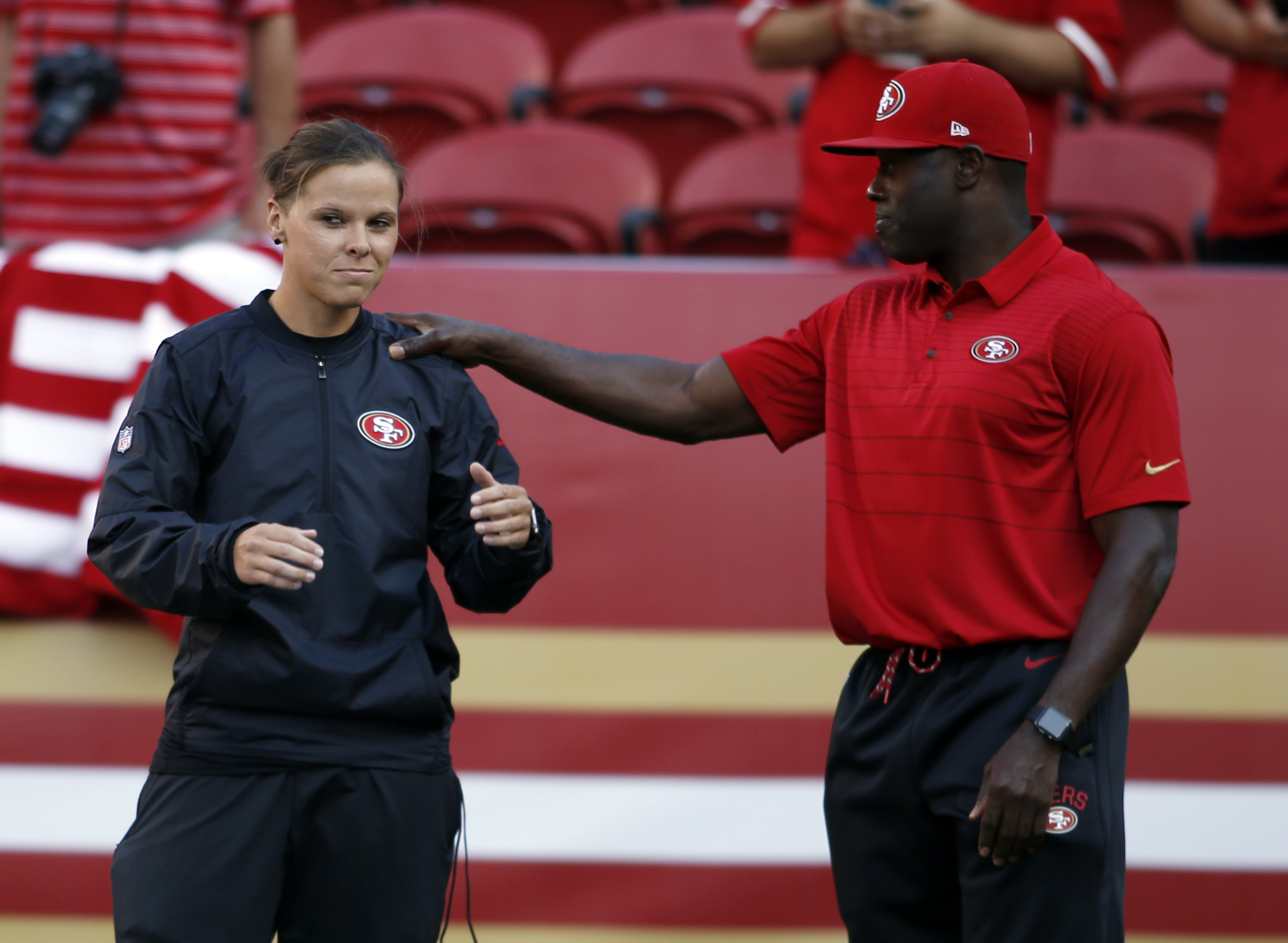 San Francisco 49ers assistant coach Katie Sowers, left, talks with a fellow coach before a preseason NFL football game against the Denver Broncos Saturday, Aug. 19, 2017, in Santa Clara, Calif. (AP Photo/D. Ross Cameron)