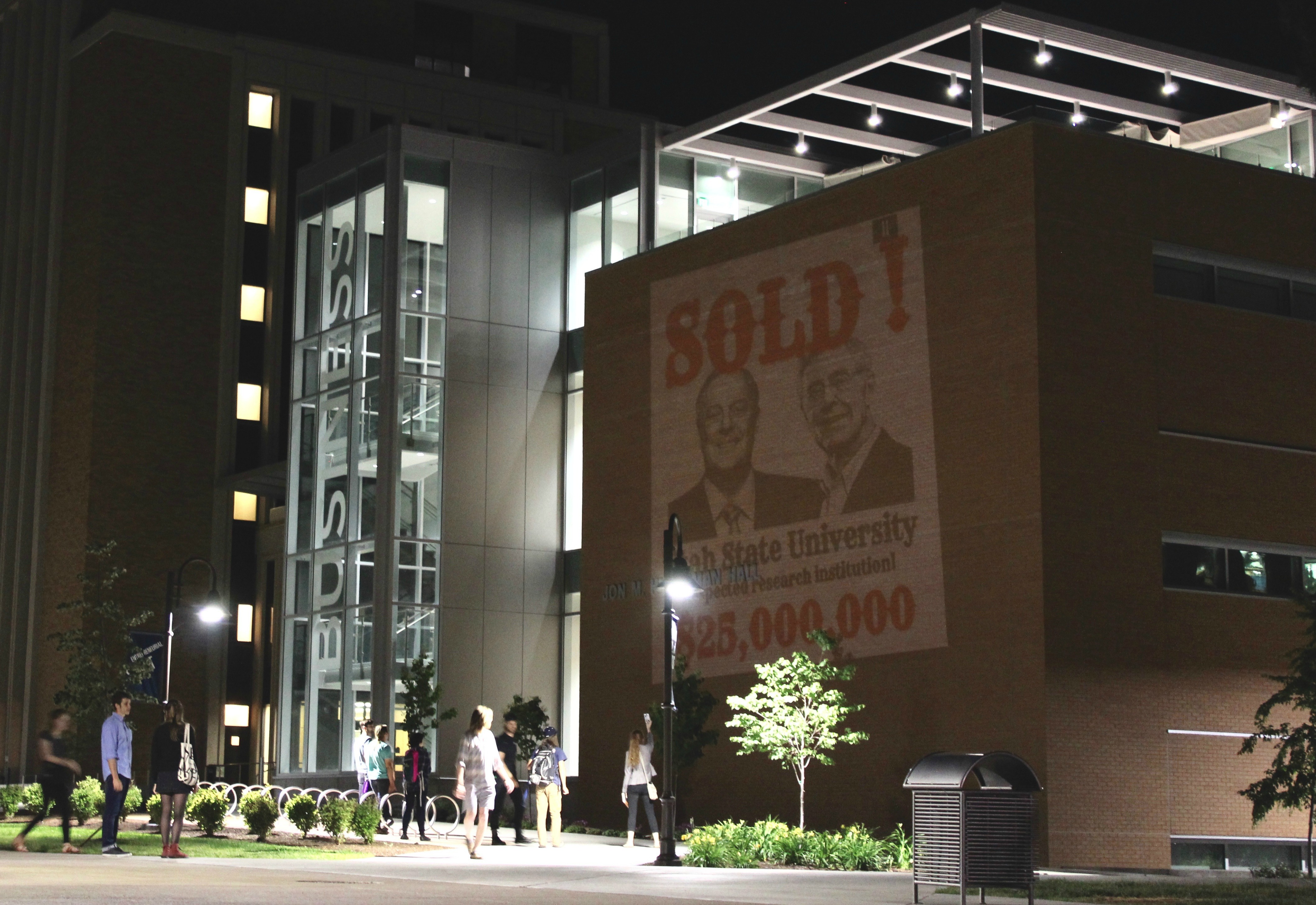 UTAH STATE UNIVERSITY STUDENTS PROJECT MESSAGE ON SIDE OF BUSINESS SCHOOL BUILDING. CREDIT: UNKOCH MY CAMPUS/GREENPEACE