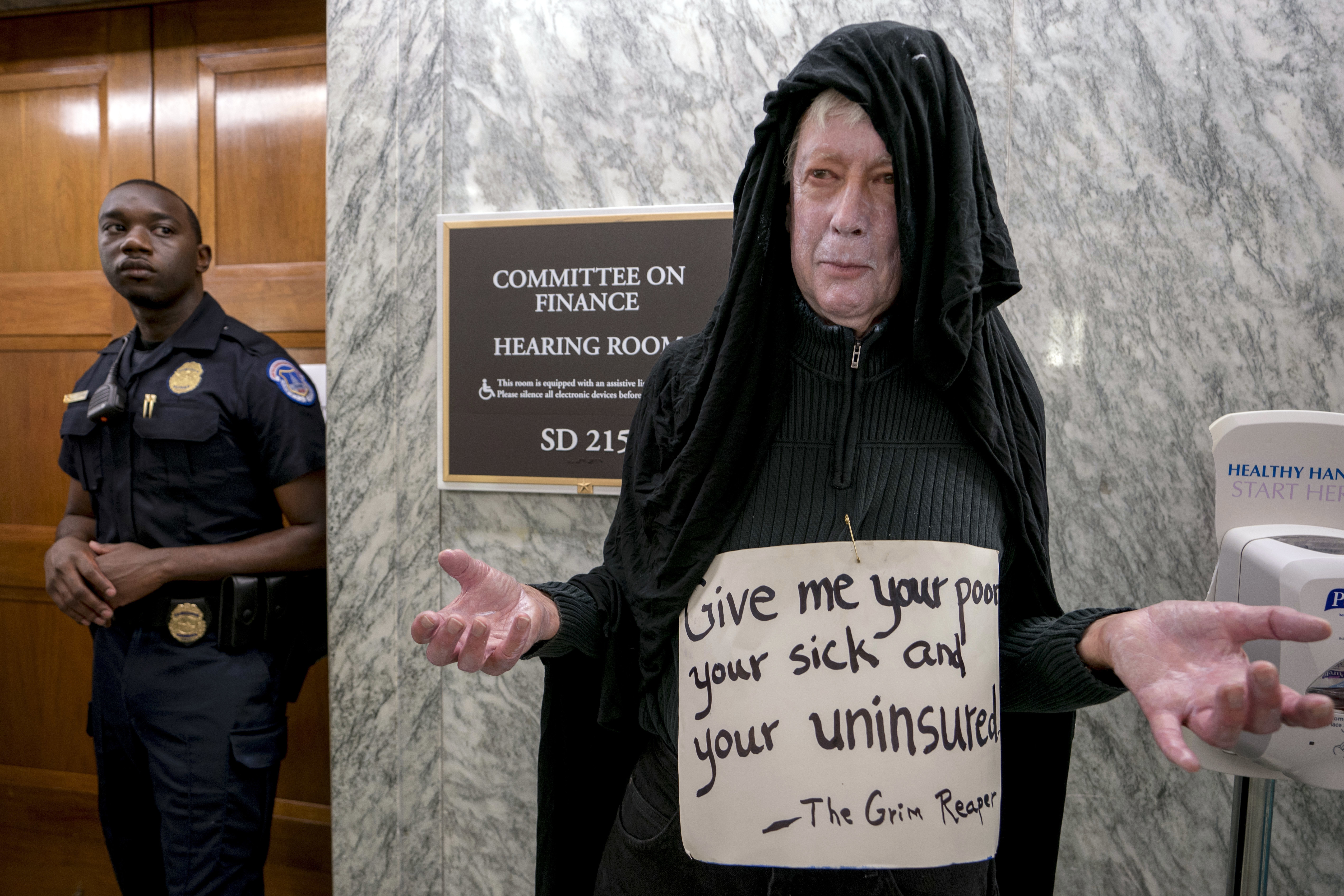 David Barrows of Washington dresses as the grim reaper and wears a sign that reads "Give me your poor, your sick, and your uninsured" as he joins others outside a hearing room where the Senate Finance Committee will hold a hearing to consider the Graham-Cassidy healthcare proposal, on Capitol Hill, Monday, Sept. 25, 2017, in Washington. CREDIT: AP Photo/Andrew Harnik