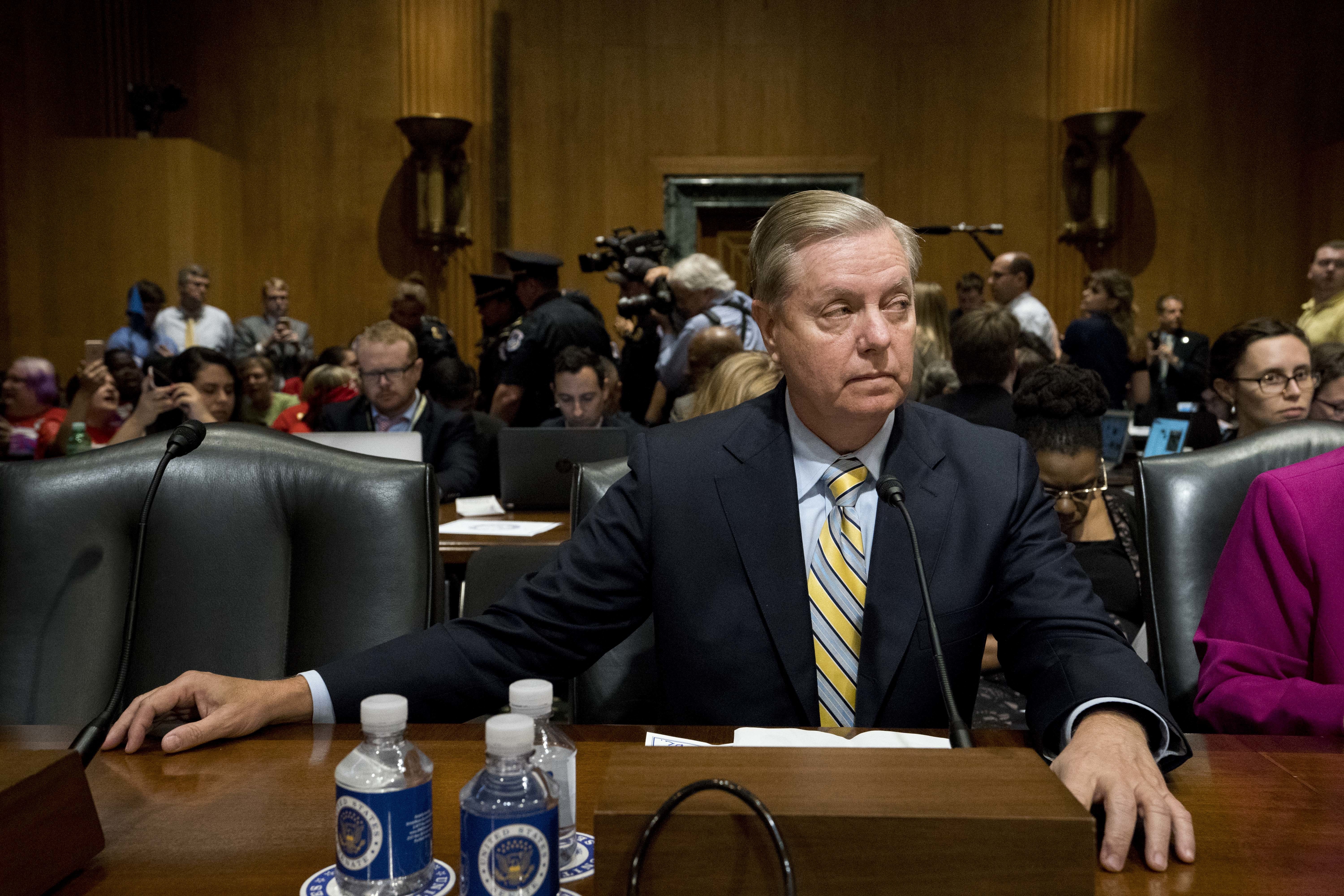 Sen. Lindsey Graham, R-S.C. waits as people in wheelchairs are removed after disrupting a Senate Finance Committee hearing to consider the Graham-Cassidy healthcare proposal, on Capitol Hill, Monday, Sept. 25, 2017, in Washington. CREDIT: AP Photo/Andrew Harnik