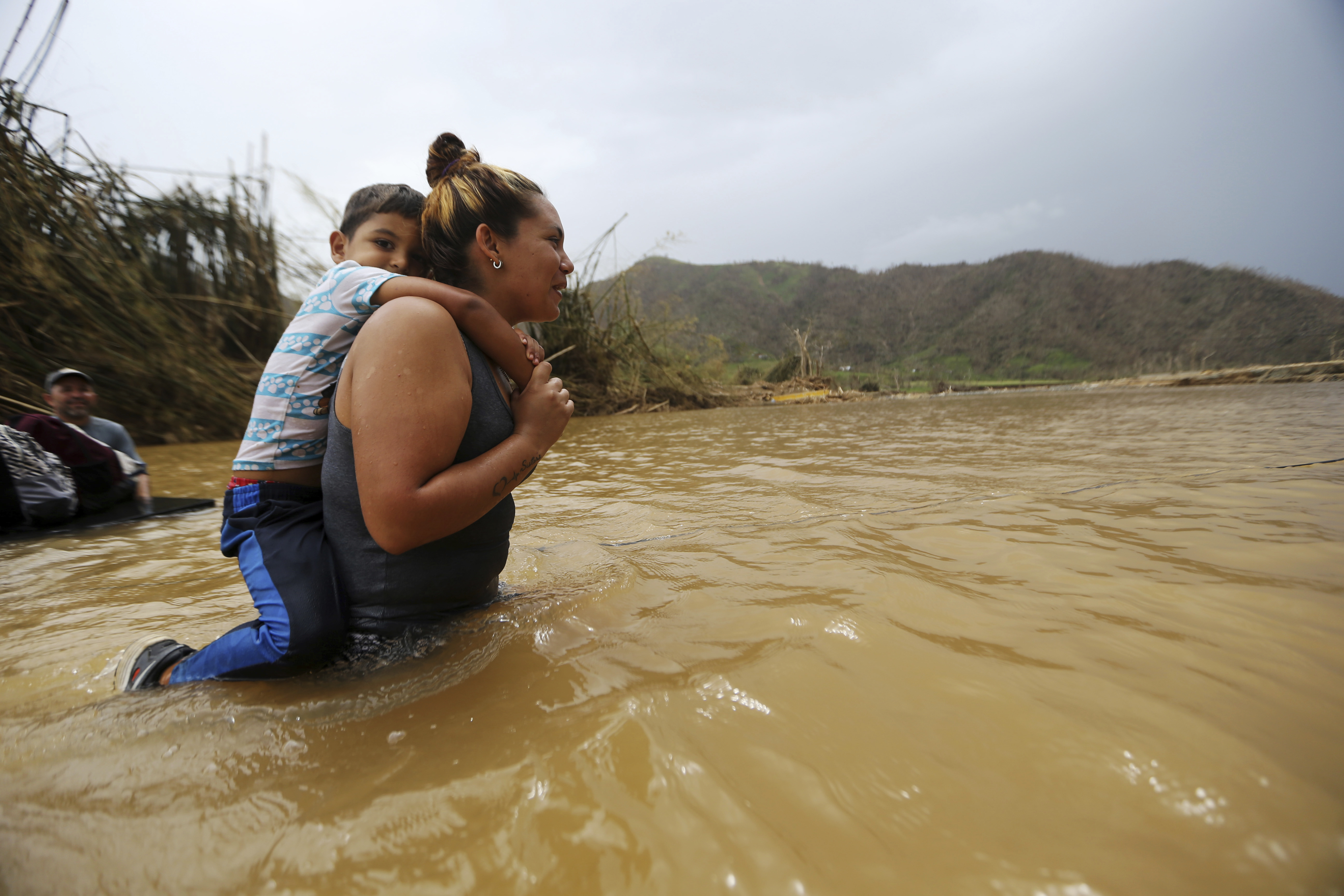 Marlene Ojeda carries her son through a river after the bridge was swept away by Hurricane Maria. (Credit: AP Photo/Gerald Herbert)
