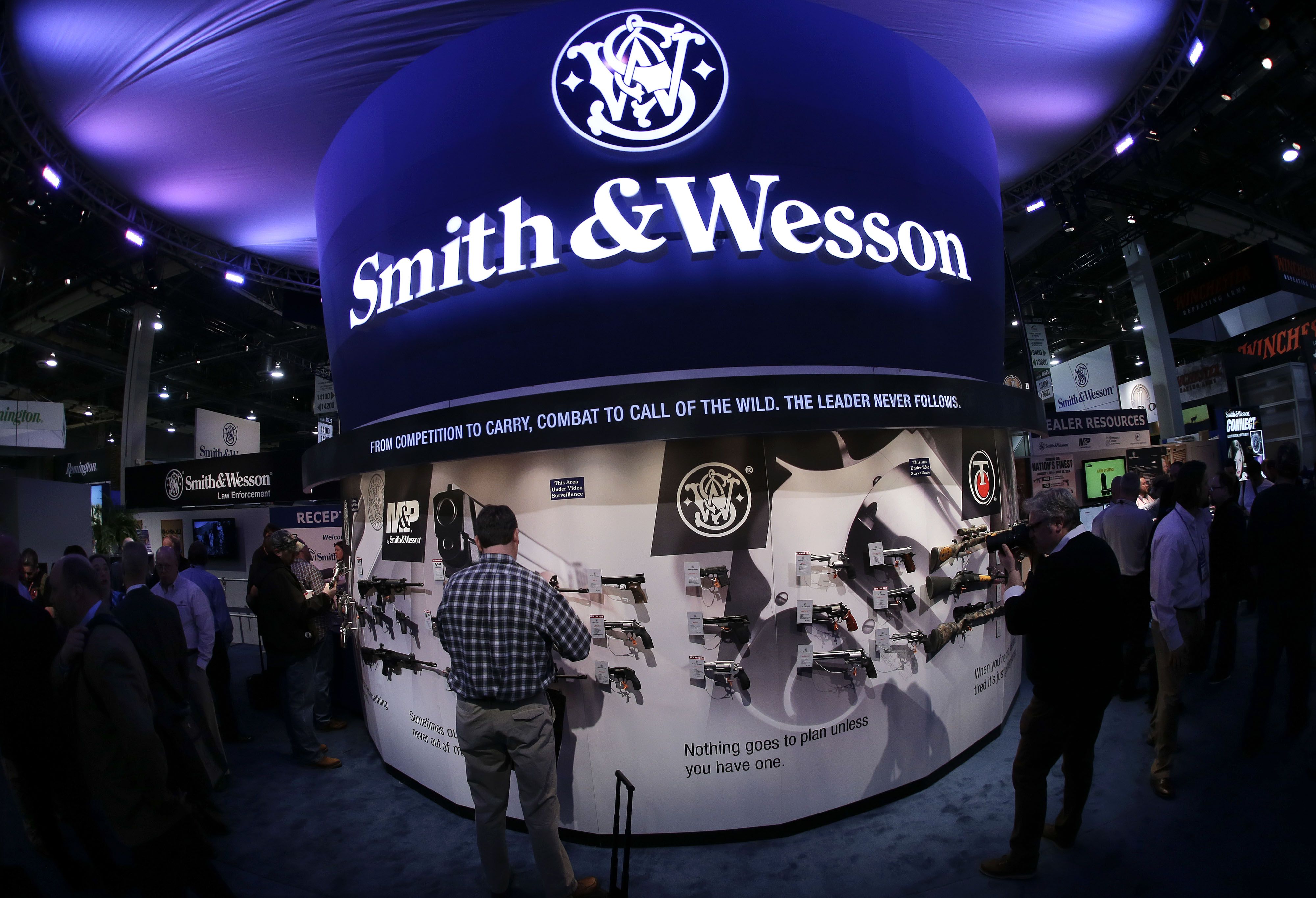 In this Tuesday, Jan. 14, 2014, file photo, trade show attendees examine handguns and rifles in the Smith & Wesson display booth at the Shooting Hunting and Outdoor Tradeshow, in Las Vegas. Nevada. Smith & Wesson changed its name to American Outdoor Brands Corp. in November 2016 to better represent its broader product offering. (Credit: AP Photo/Julie Jacobson, File)