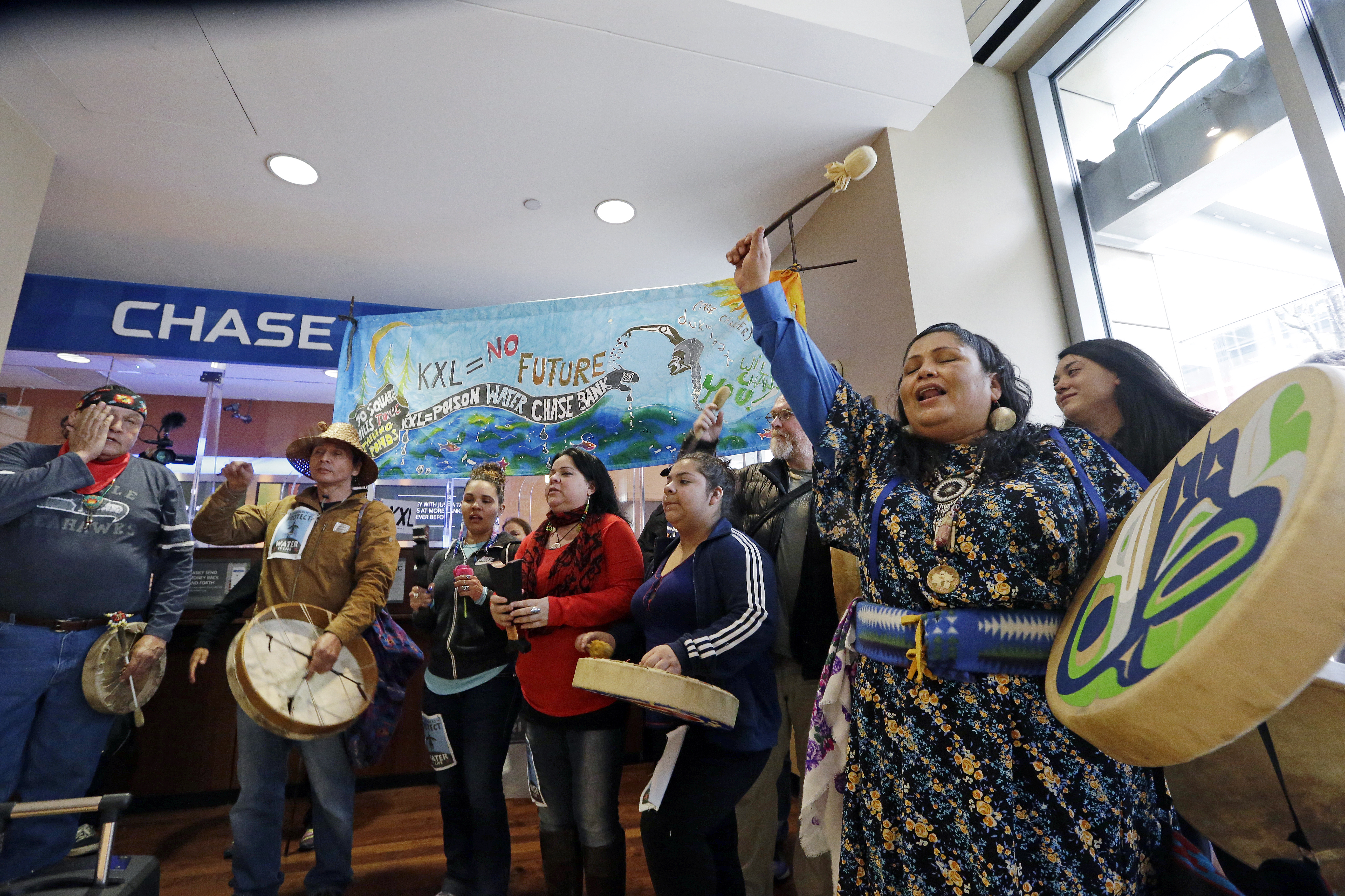 Roxanne White, right, a member of the Yakama Nation, sings with other Native Americans during a protest inside a Chase bank branch Monday, May 8, 2017, in Seattle. CREDIT: AP Photo/Elaine Thompson
