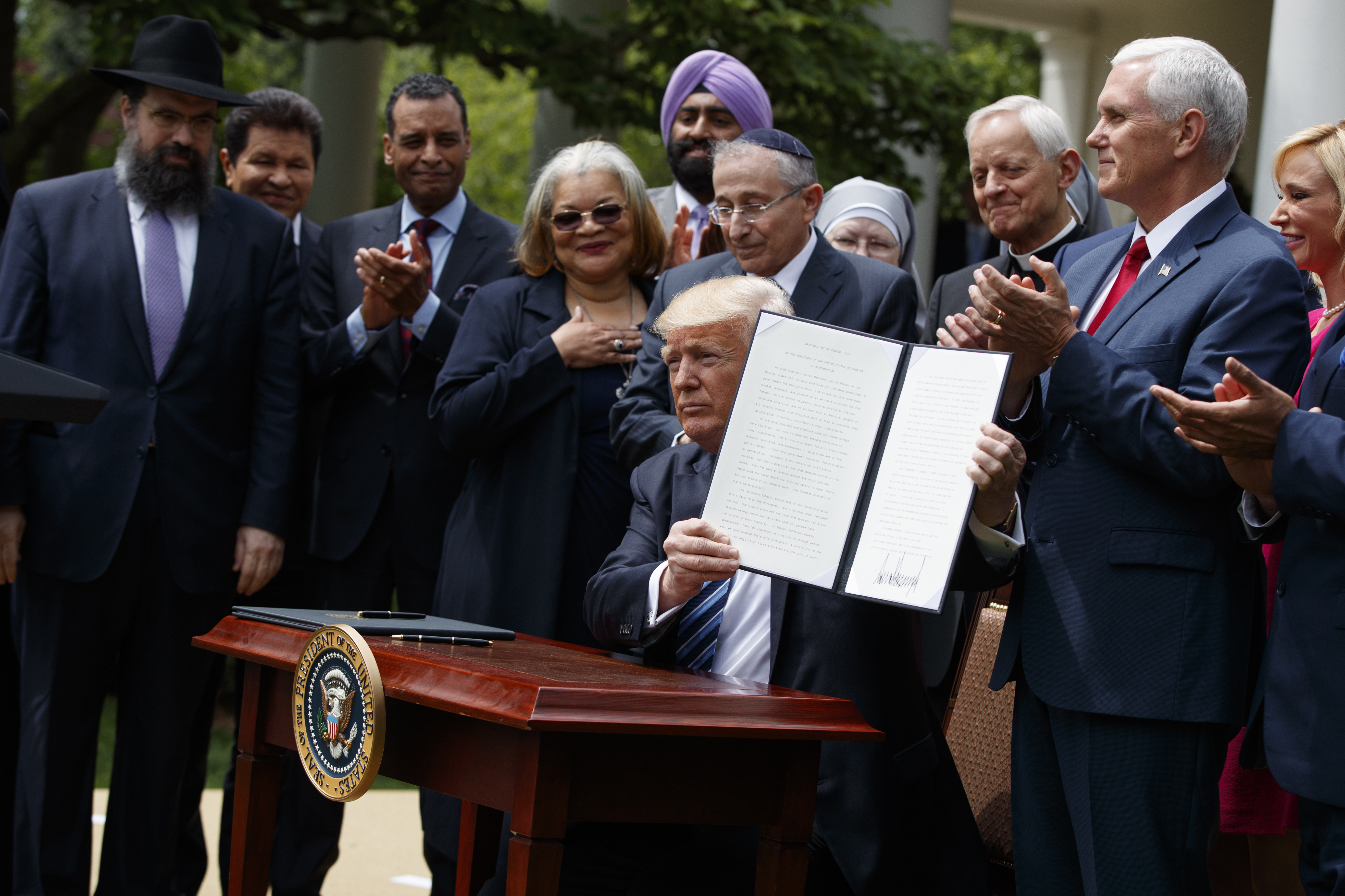 President Donald Trump, flanked by clergy and some of his faith advisers, holds up a signed executive order on "religious liberty" in May. CREDIT: AP Photo/Evan Vucci