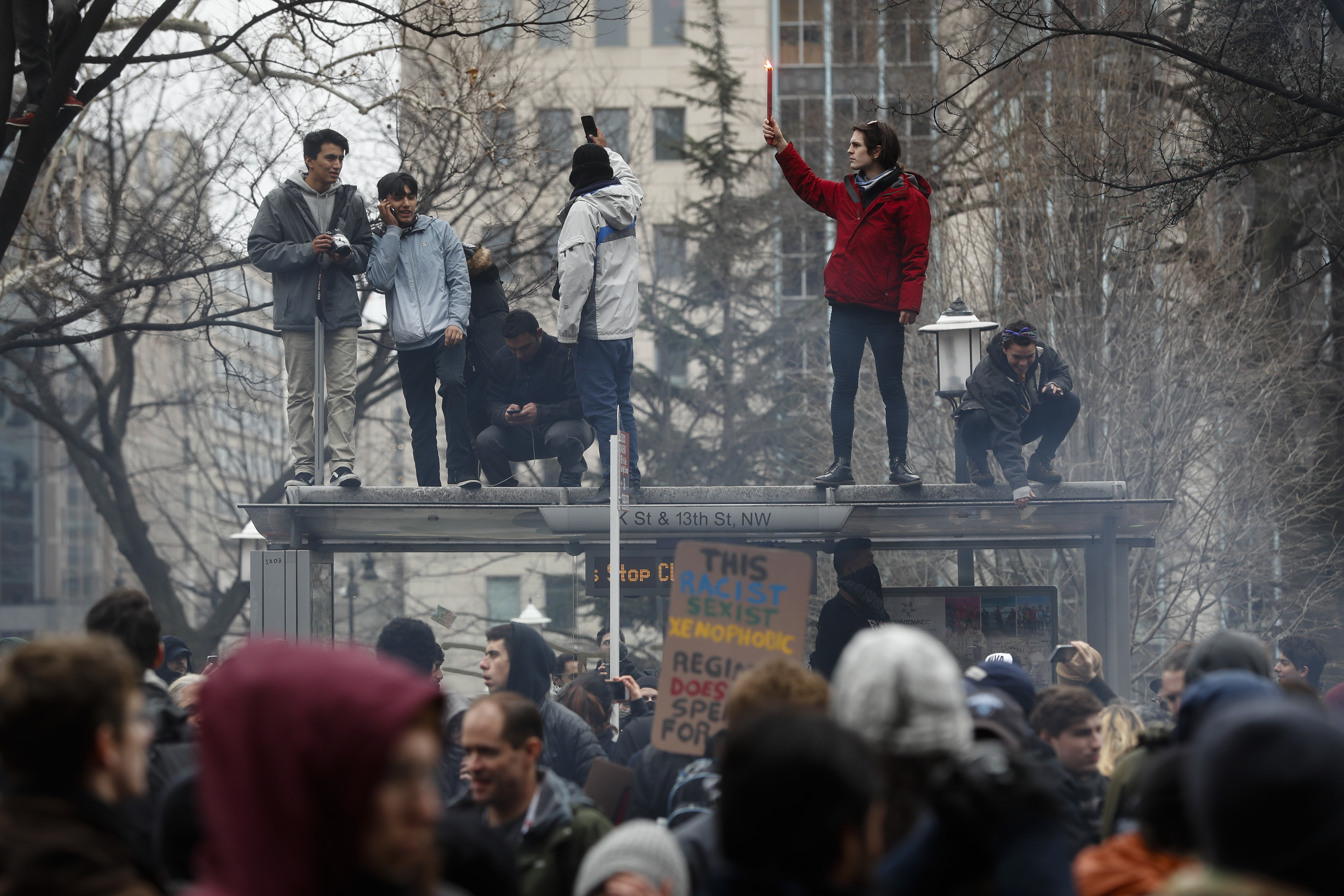 Protesters stand on a bus shelter during a demonstration after the inauguration of President Donald Trump, Friday, Jan. 20, 2017, in Washington. (CREDIT: AP Photo/John Minchillo)
