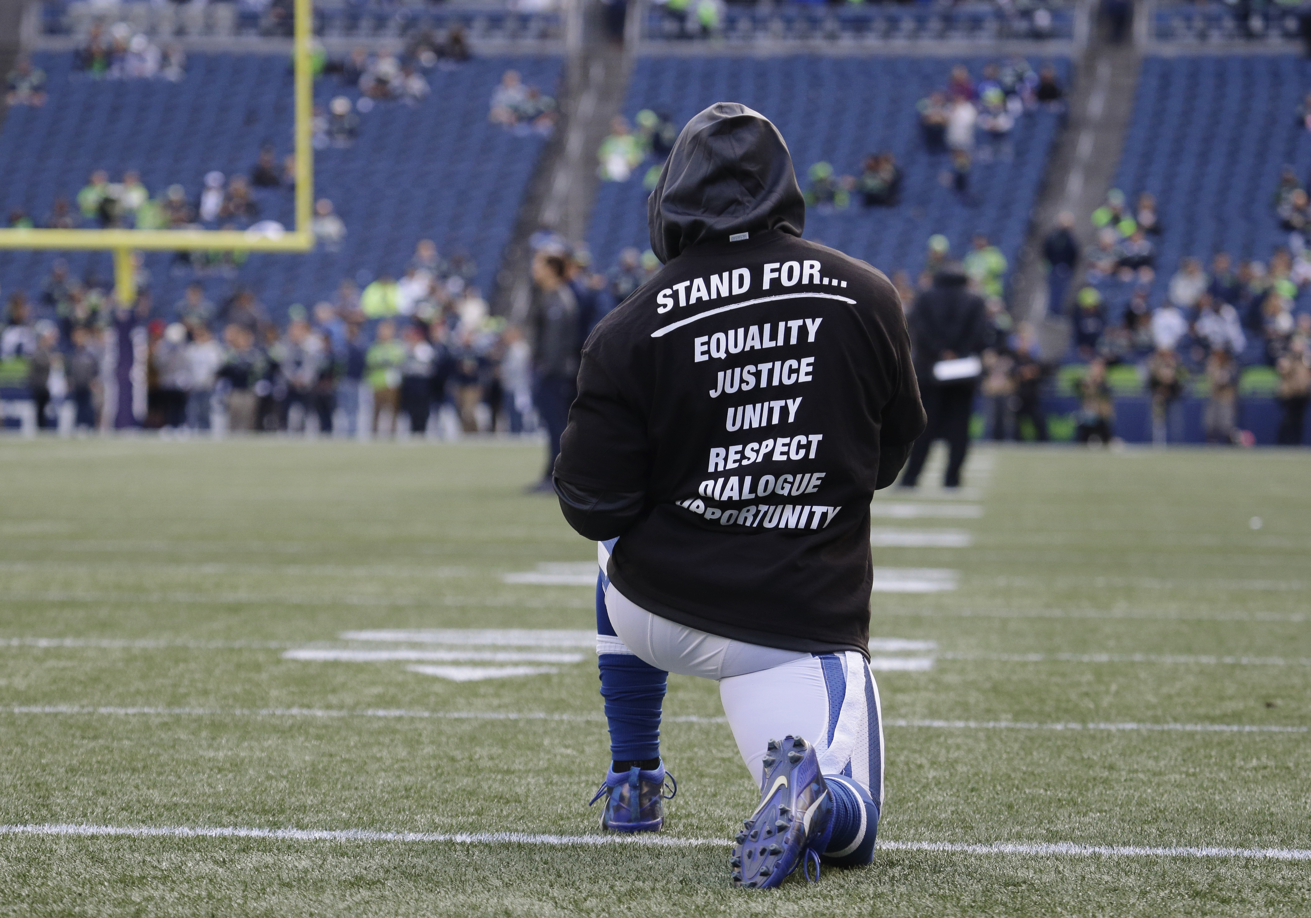 An Indianapolis Colt player kneels on the field Sunday, Oct. 1, 2017, during warmups before an NFL football game against the Seattle Seahawks in Seattle. The unidentified player is wearing a special team t-shirt in reference to recent protests during the singing of the national anthem at NFL football games. (AP Photo/Elaine Thompson)