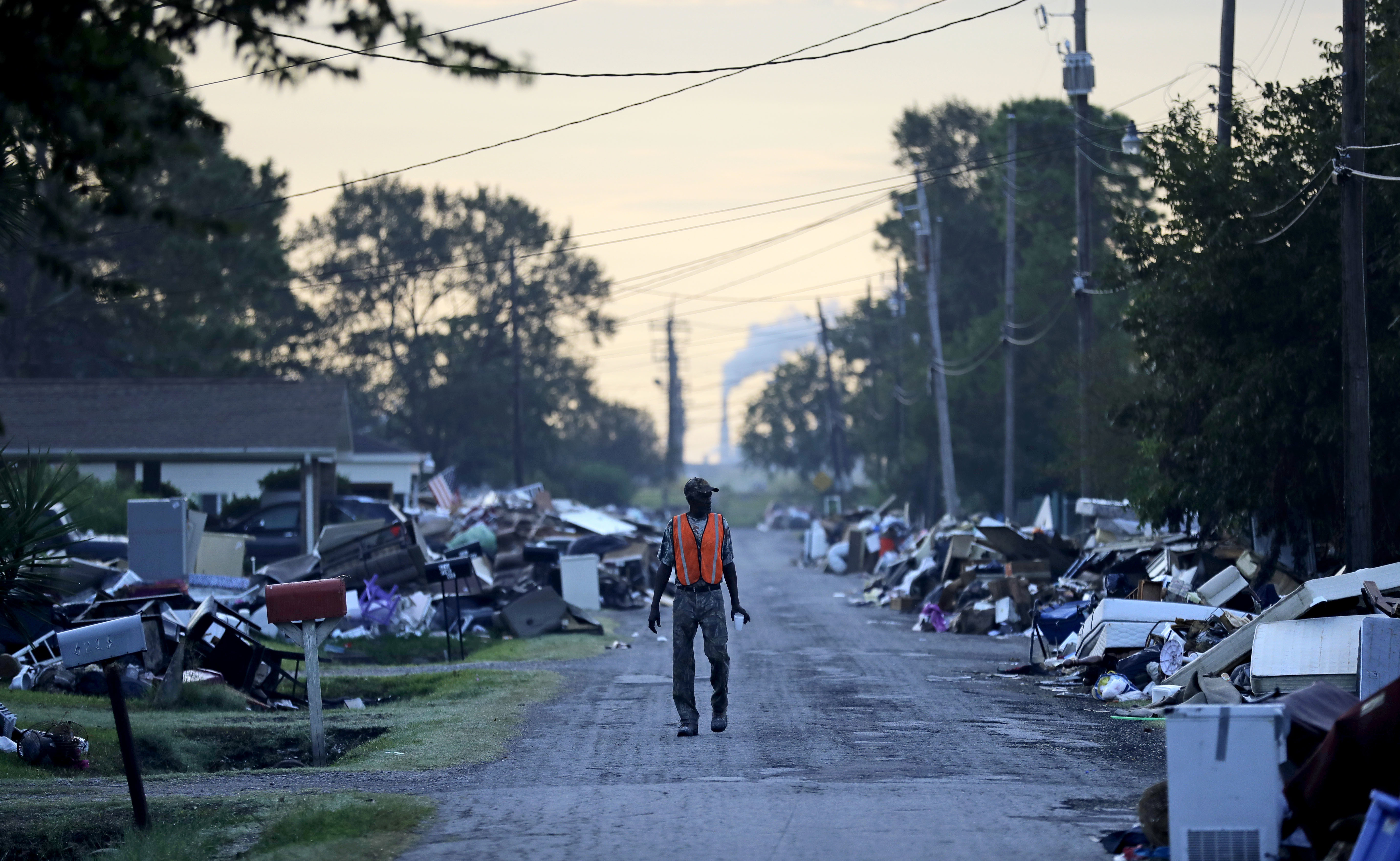 A man walks past debris from homes on his street damaged in flooding from Hurricane Harvey as an oil refinery stands in the background in Port Arthur, Texas, Thursday, Sept. 28, 2017. (AP Photo/David Goldman)