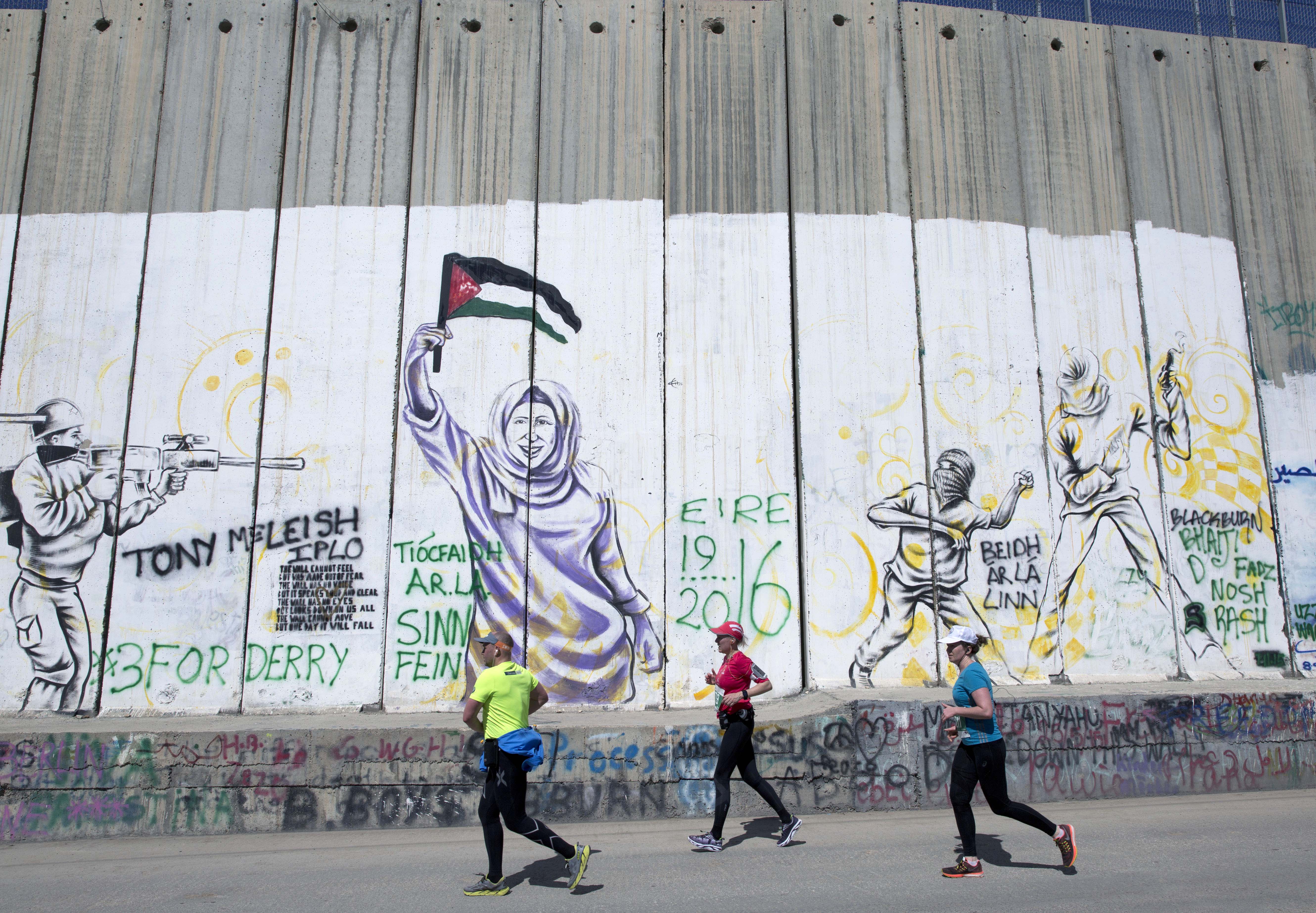 Runners taking part in the Palestine Marathon pass by the Israeli separation barrier in the West Bank city of Bethlehem, Friday, April 1, 2016. CREDIT: AP Photo/Nasser Nasser
