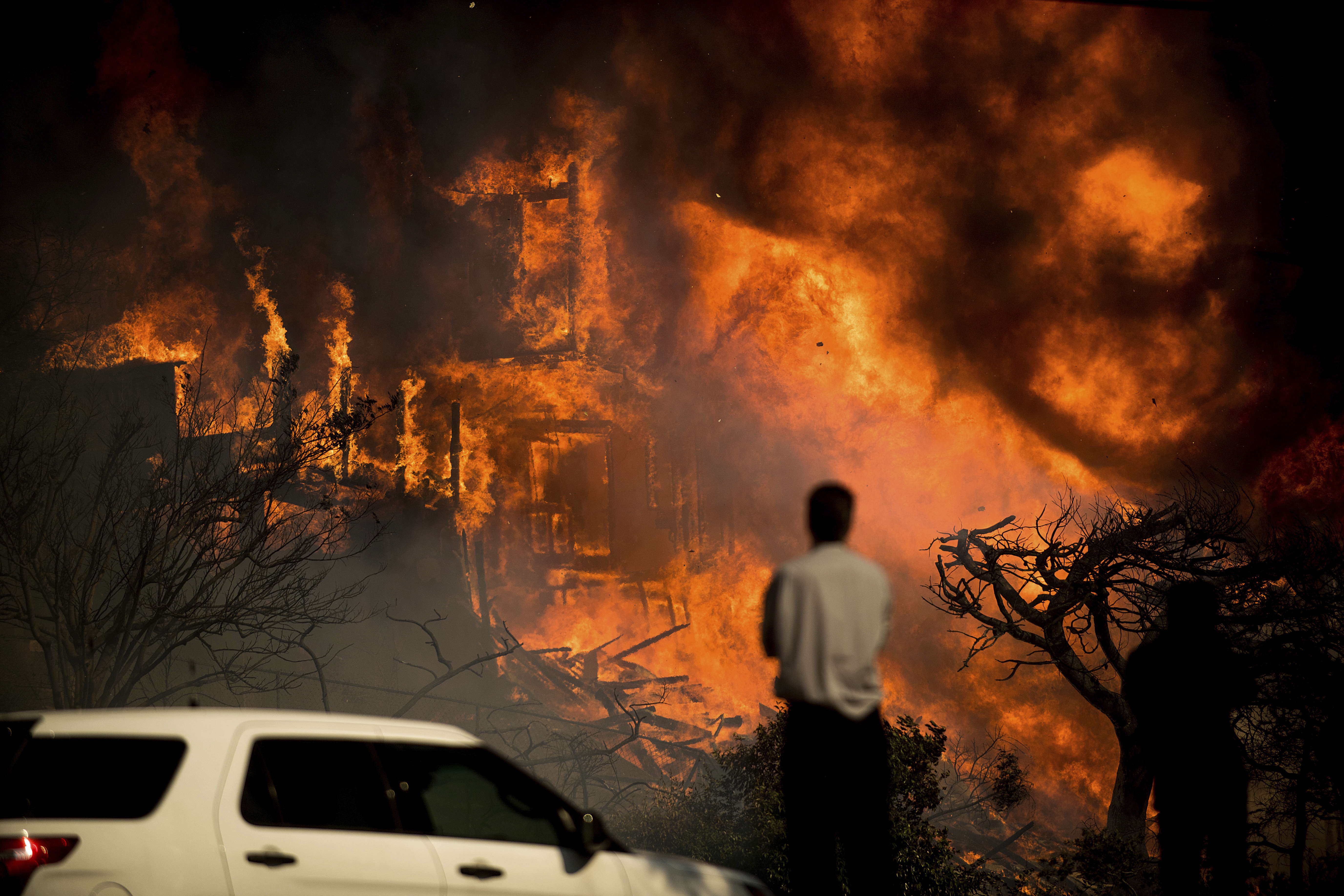 A man watches flames consume a residence as a wildfire rages in Ventura, California on December 5, 2017. CREDIT: AP Photo/Noah Berger