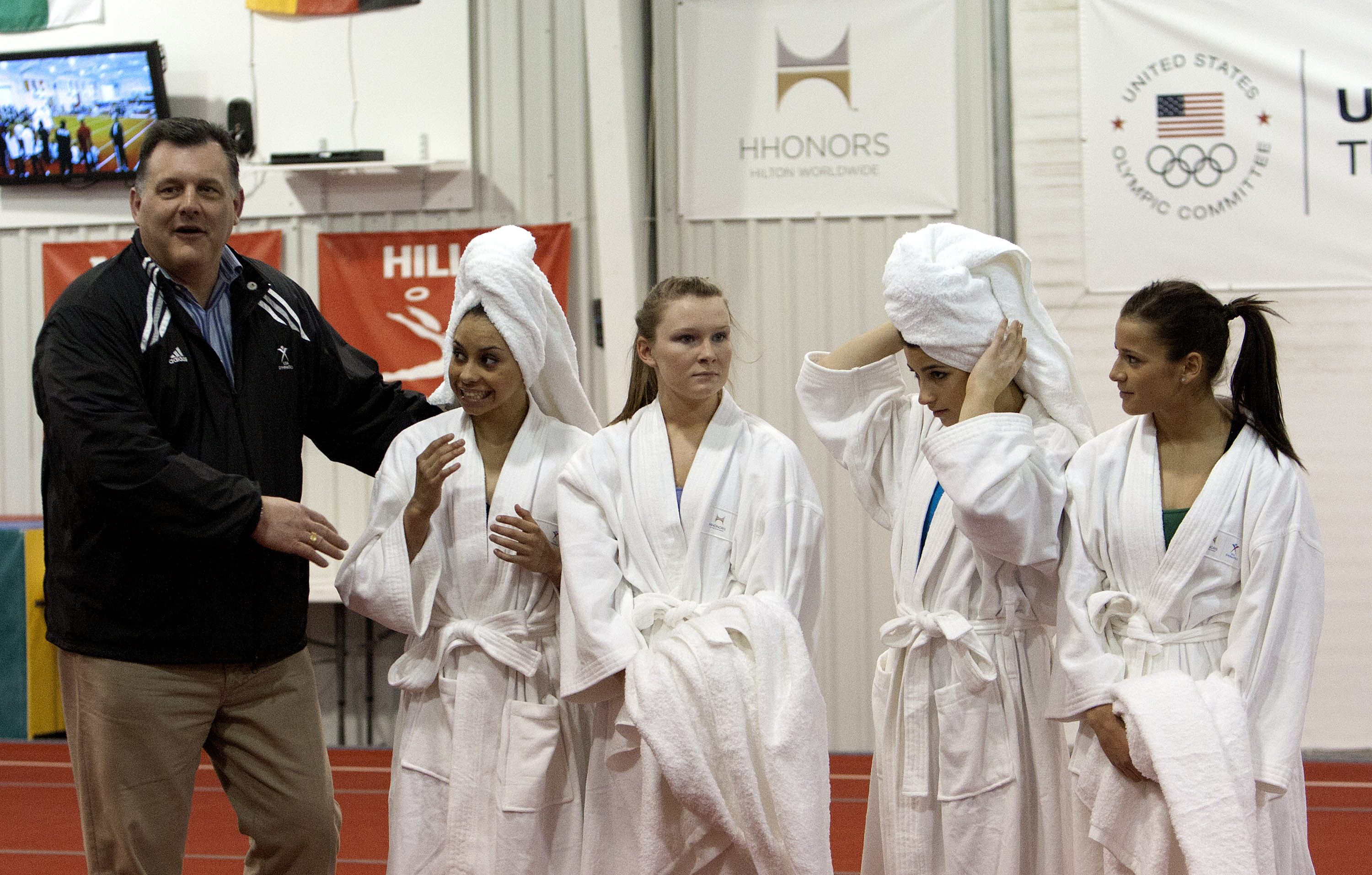(L-R) Steve Penny, President and CEO of USA Gymnastics introduces Mattie Larson, Bridget Sloane, Alexandria Raisman and Alicia Sacramone display their Hilton robes and towles as part of an announcement of Hilton's partnership of USA Gymnastics during a press conference at Karolyi Ranch. Photo by Bob Levey/Getty Images for Hilton