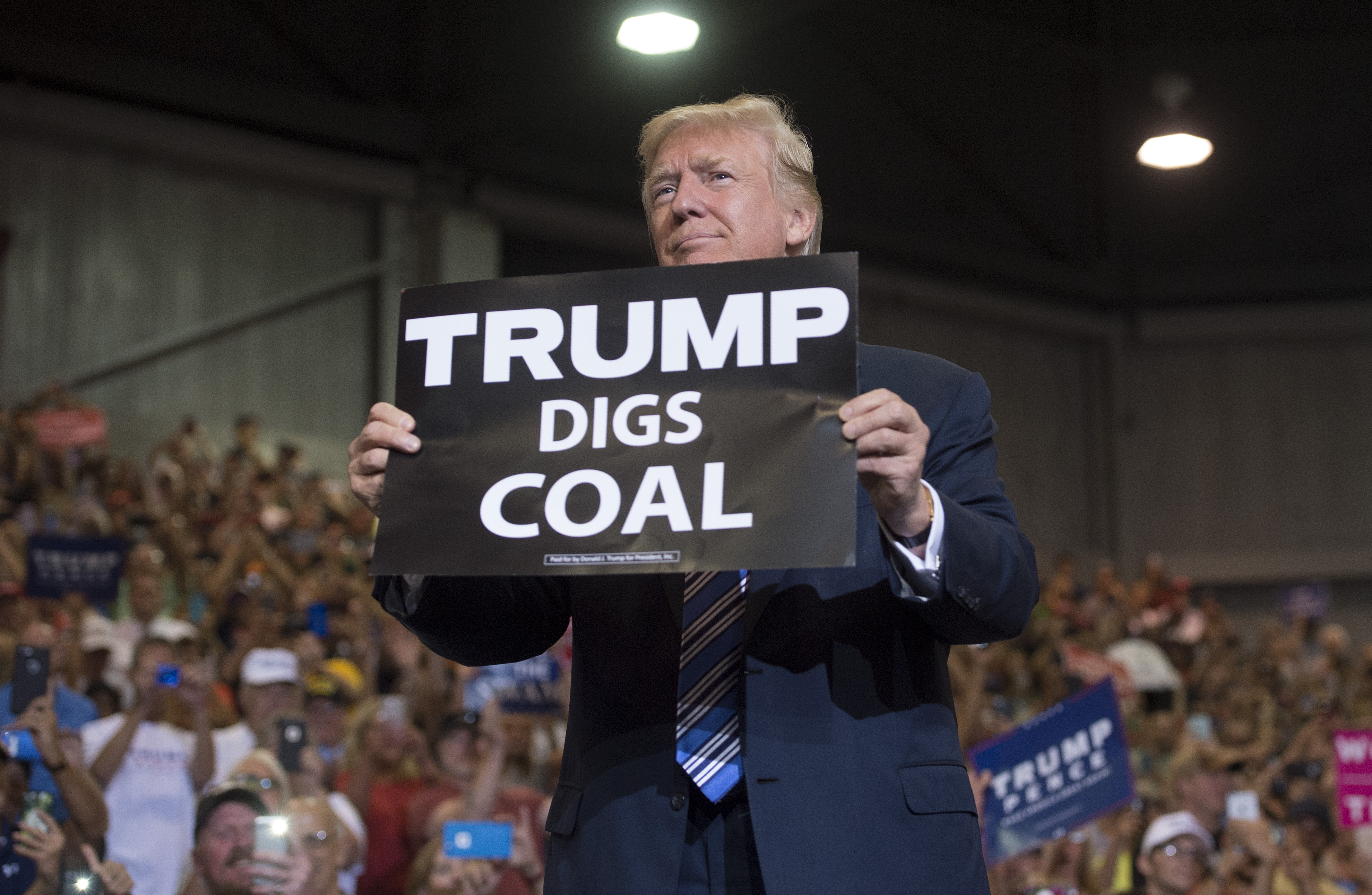 President Donald Trump holds up a "Trump Digs Coal" sign as he arrives to speak during rally in Huntington, West Virginia. CREDIT: SAUL LOEB/AFP/Getty Images