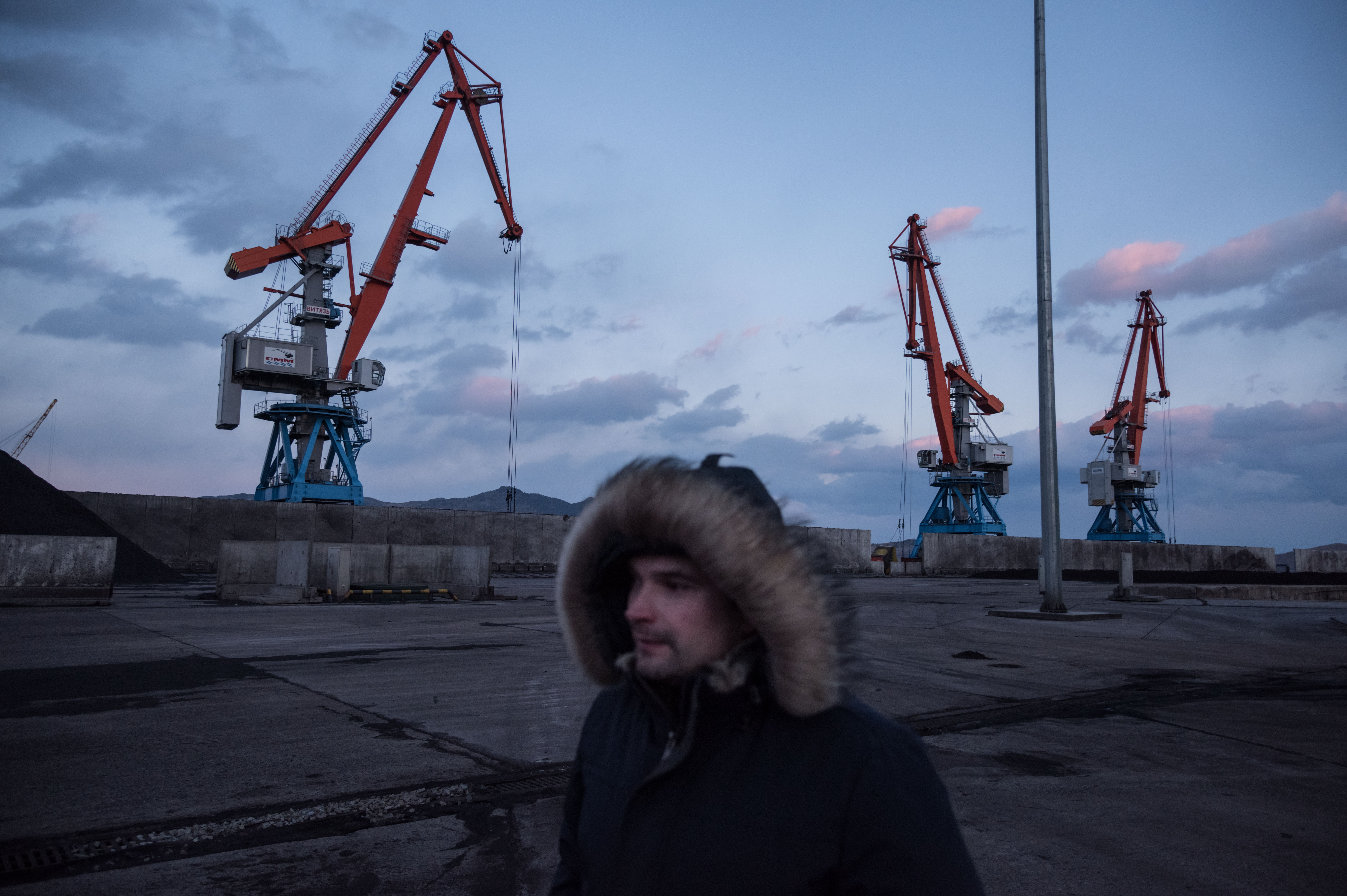 A photo taken on November 21, 2017 shows a Russian worker walking before cranes at the RasonConTrans coal port at Rajin harbour in the Rason Special Economic Zone.
A mountain of North Korean coal -- which would once have been bound for China -- is piled up on one side of the barrier in Rajin harbour, stranded by a UN ban on coal exports by Pyongyang. CREDIT: Ed Jones //AFP/Getty Images.