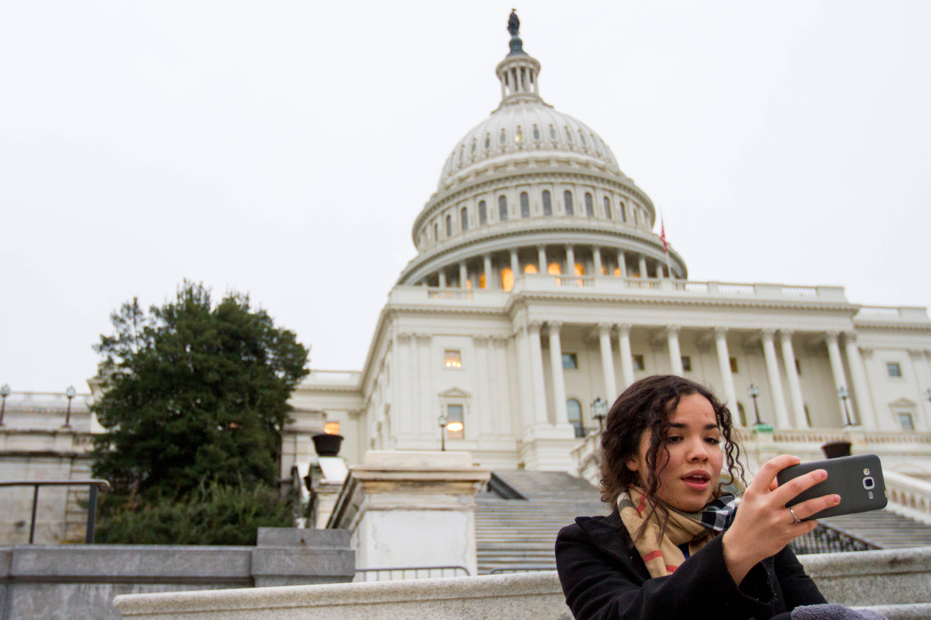 Maria sits alone on the steps of the U.S. Capitol, filming a video of herself asking people to donate so more DACA recipients can tell their stories at the Capitol on Dec. 8, 2017. (Credit: Megan Janetsky)