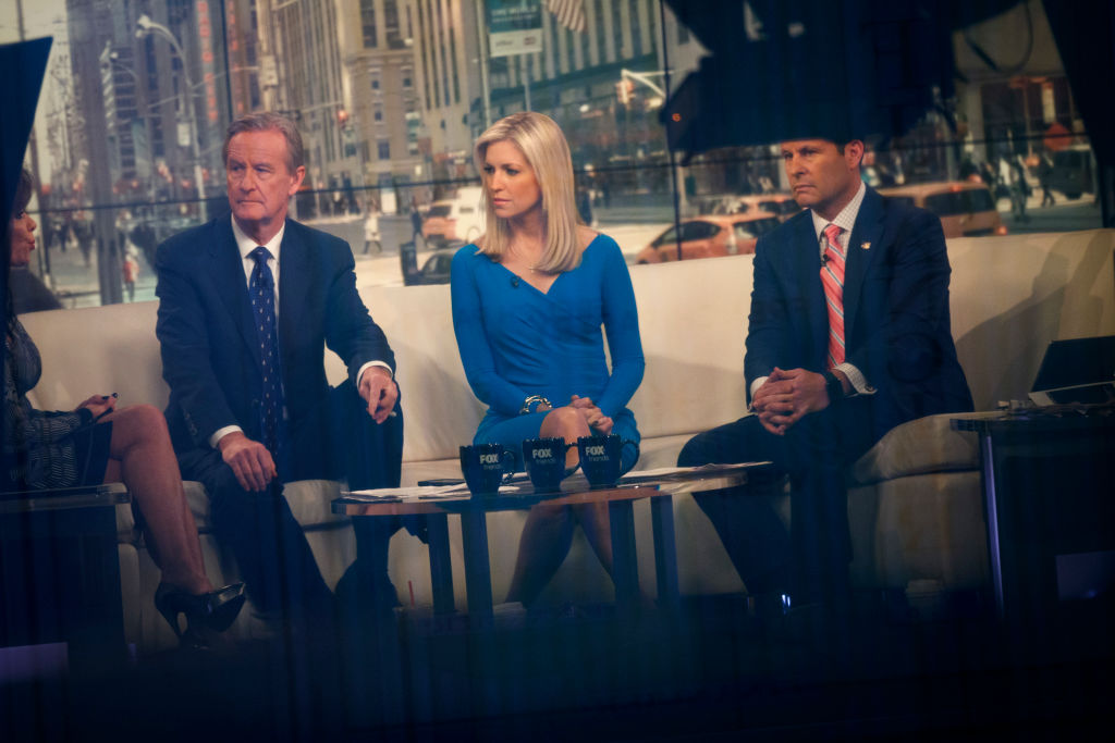 Seen through a window, (L to R) hosts Steve Doocy, Ainsley Earhardt, and Brian Kilmeade broadcast 'Fox And Friends' from the Fox News studios, February 17, 2017 in New York City. CREDIT: Drew Angerer/Getty Images