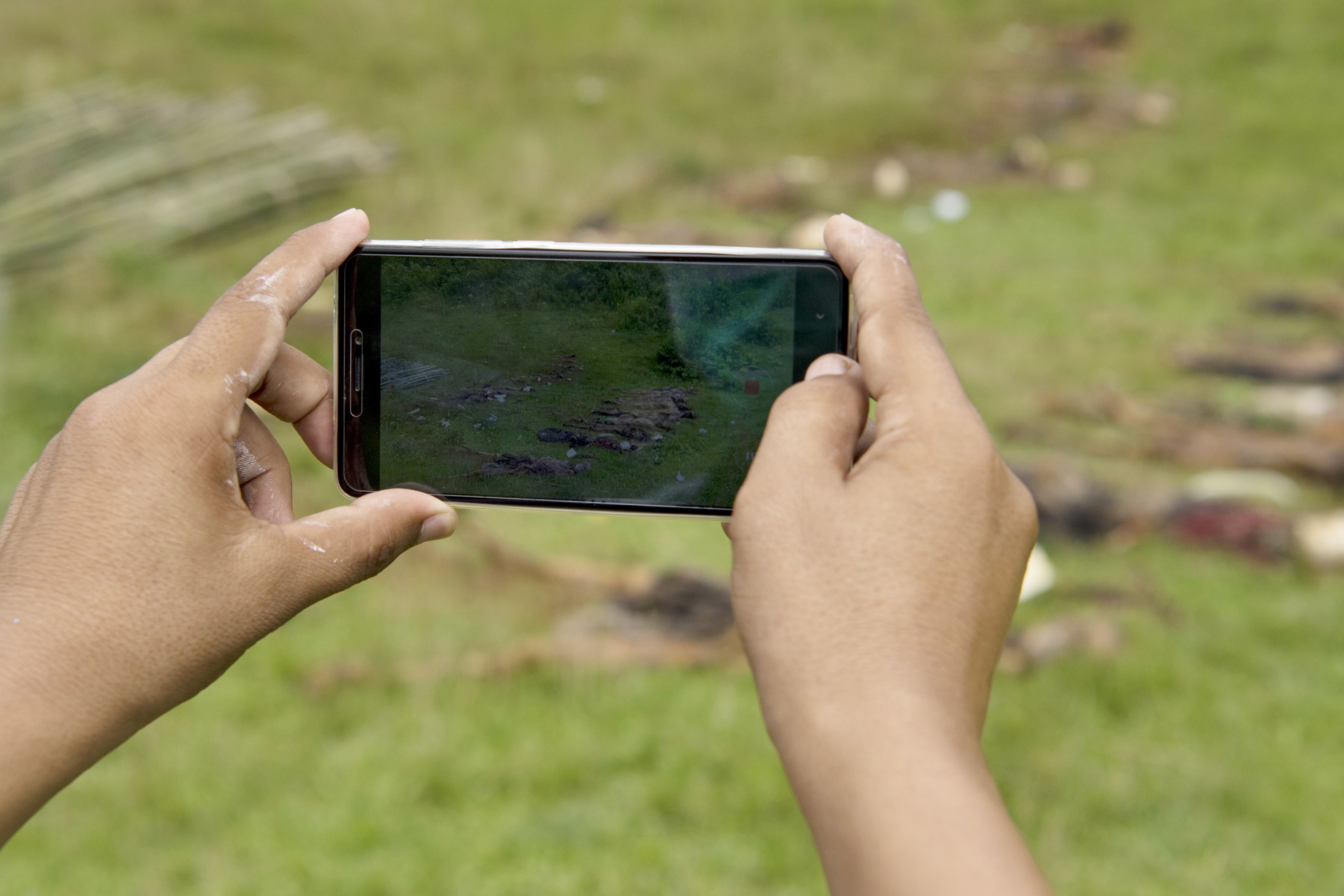 A man takes photos with a mobile phone of the dead bodies in Yebawkya village, Maungdaw on September 27, 2017.
Myanmar's army said on September 24, 2017 it had discovered a mass grave containing the bodies of 28 Hindus, including women and children, in violence-wracked Rakhine state, blaming the killings on Muslim Rohingya insurgents. CREDIT: STR /AFP/Getty Images.