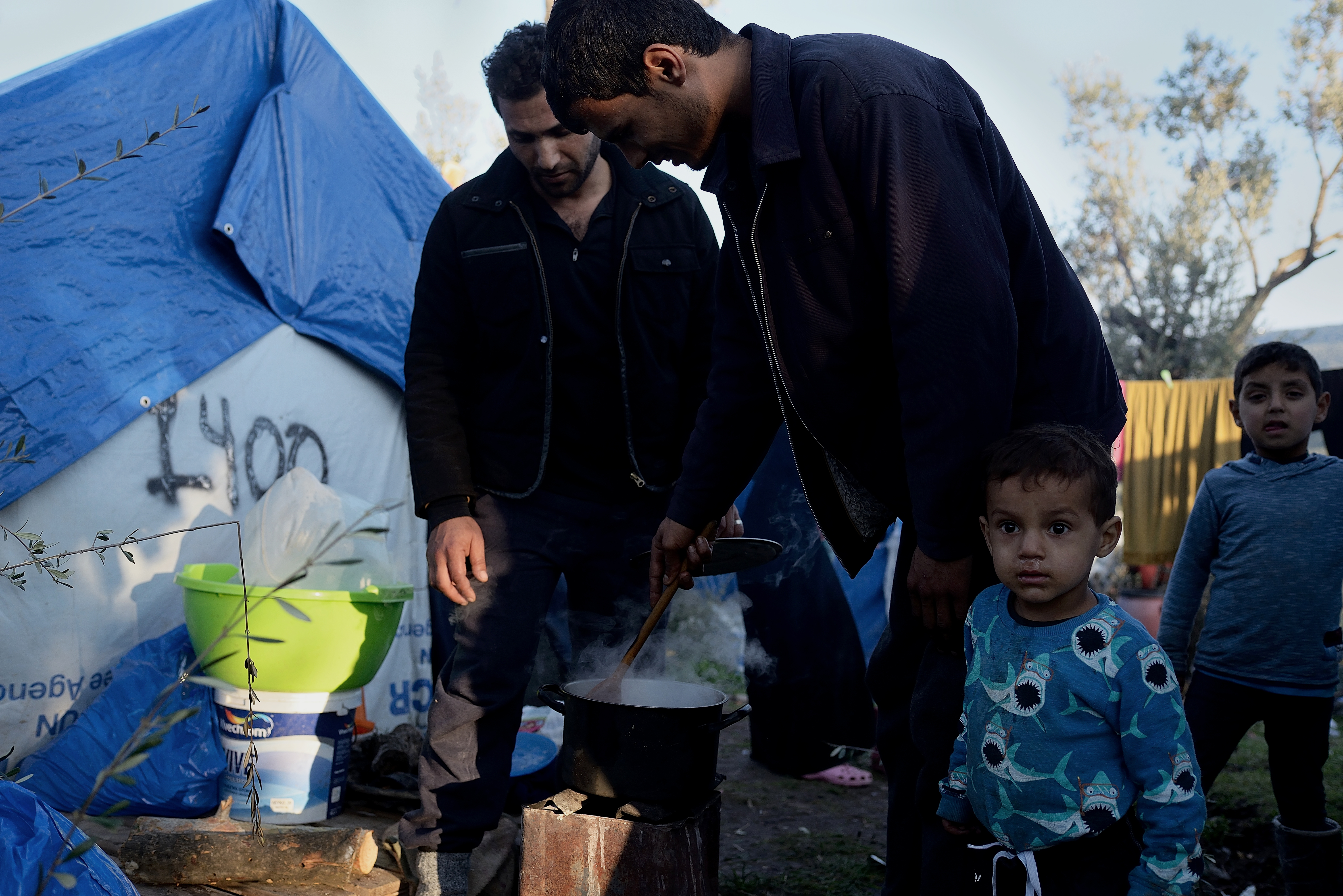 A refugee family cook with chicken broth outside the migrant and refugee registration camp in Moria, Lesbos on 6th February, 2018. CREDIT: Juan Carlos Lucas/NurPhoto via Getty Images.