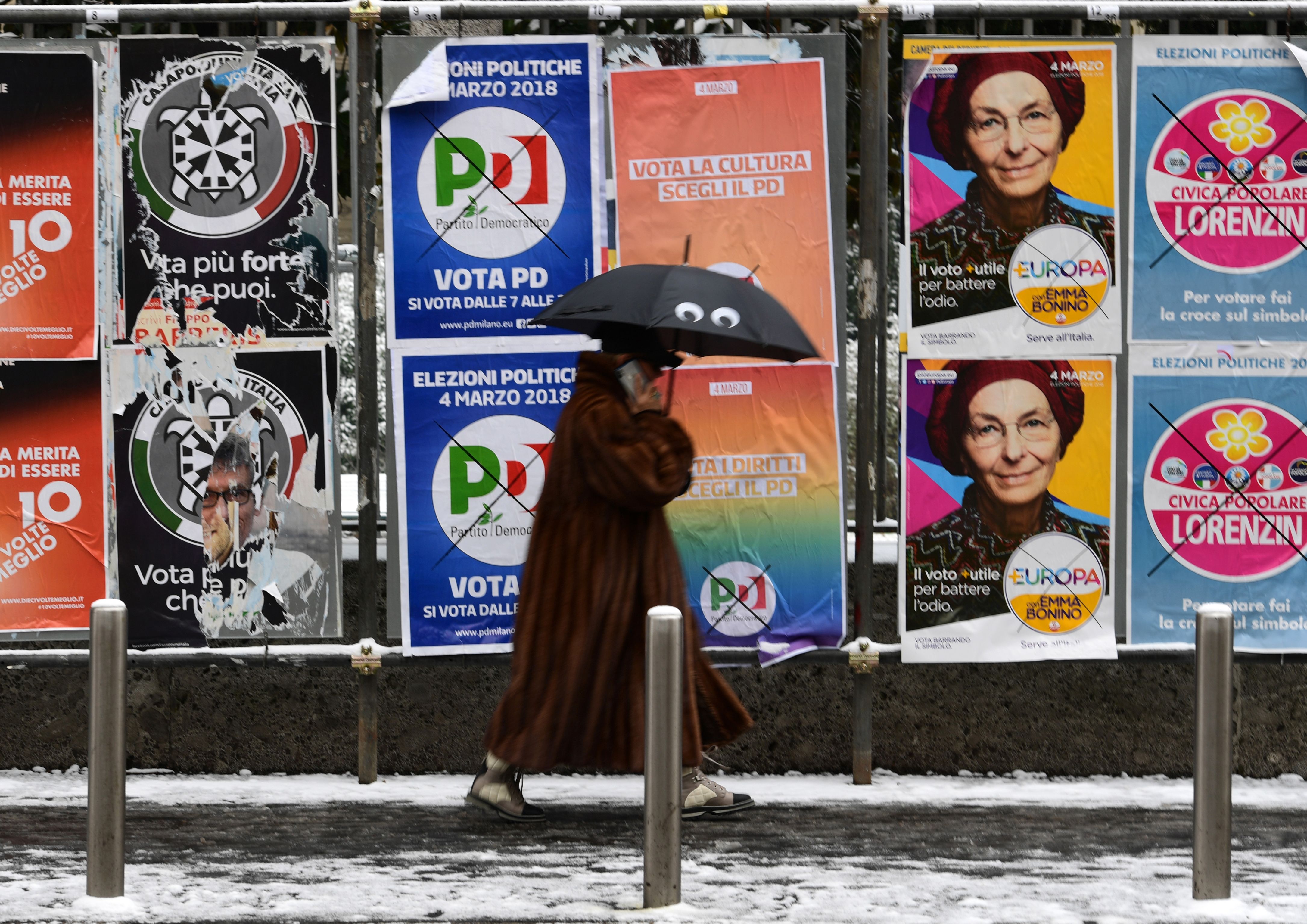 A pedestrian passes in front of election hoardings in Milan on March 1, 2018, prior to the Italian presidential elections. (credit: MIGUEL MEDINA/AFP/Getty Images)