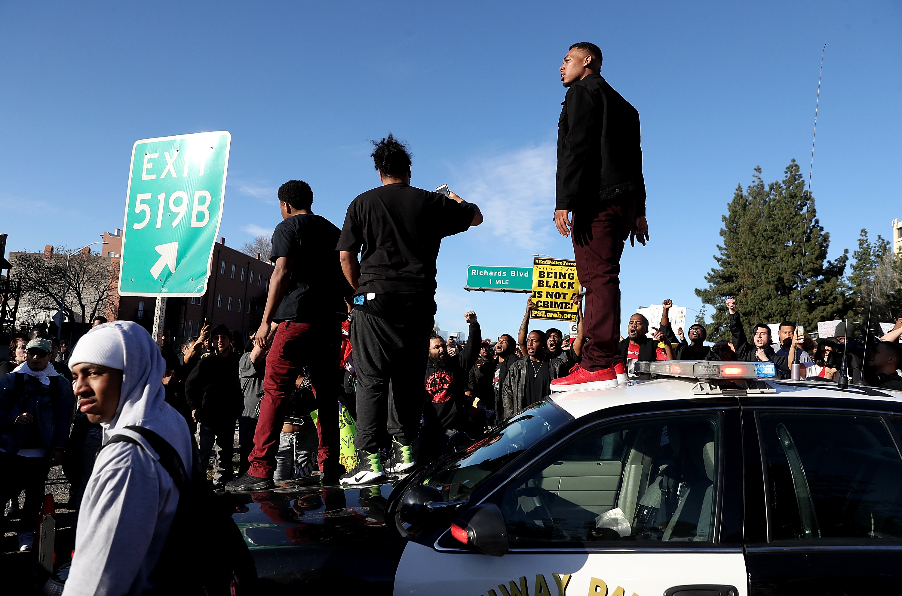 Protesters stand on a California Highway Patrol car on Interstate 5 during a human blockade of traffic days after Stephon Clark was killed by police. (CREDIT: Justin Sullivan/Getty Images)