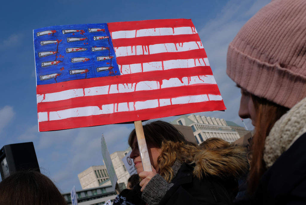 FILE PICTURE: A woman holds a sign with an American flag dripping red and its stars replaced by bullets while protesting at the "March for our Lives" gathering on March 24, 2018 in Berlin, Germany. (Photo by Sean Gallup/Getty Images)