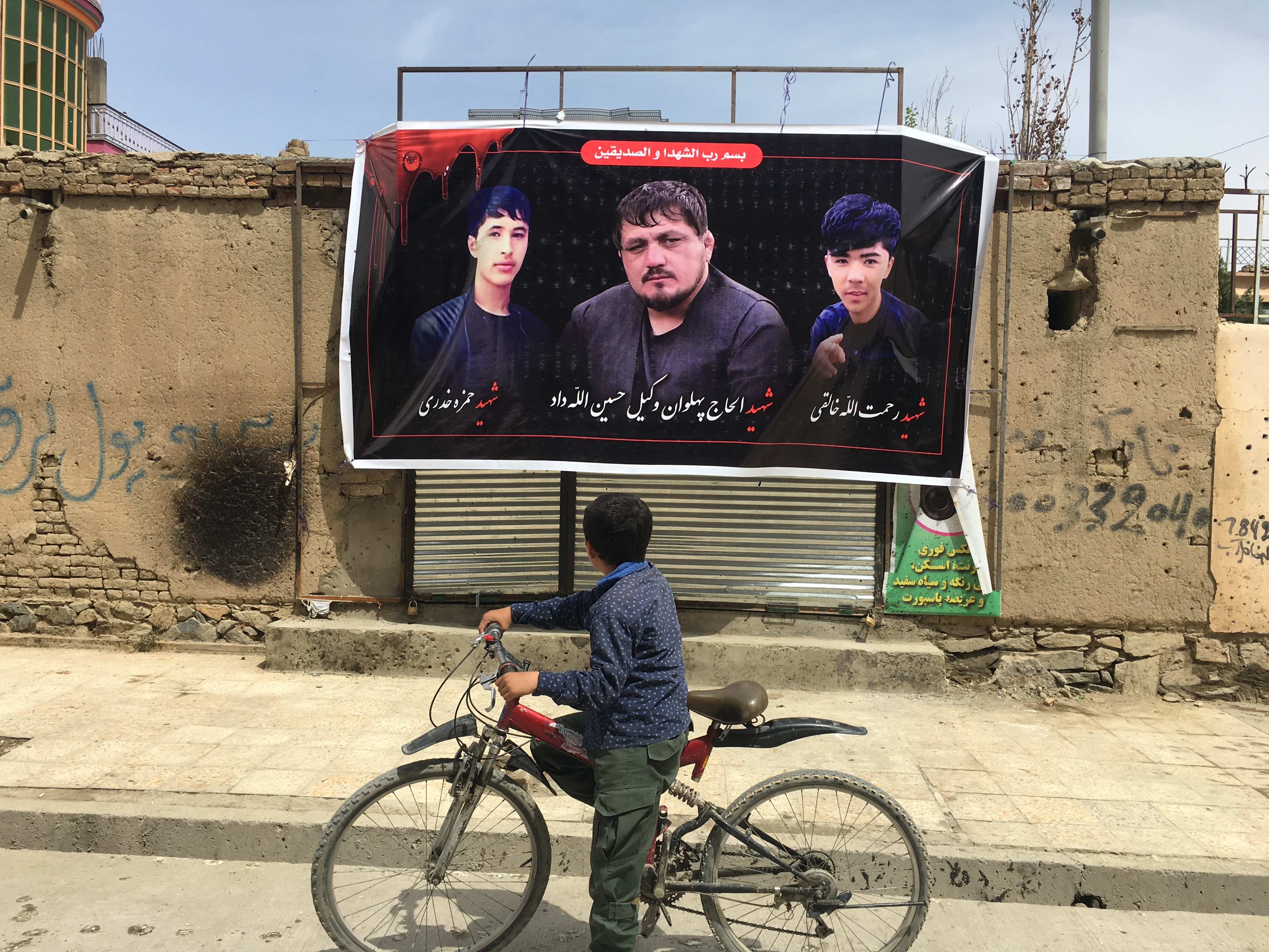 An Afghan child stops in front of a sign displaying photos of martyrs killed in recent attacks. (Credit: Ali Latifi for ThinkProgress)