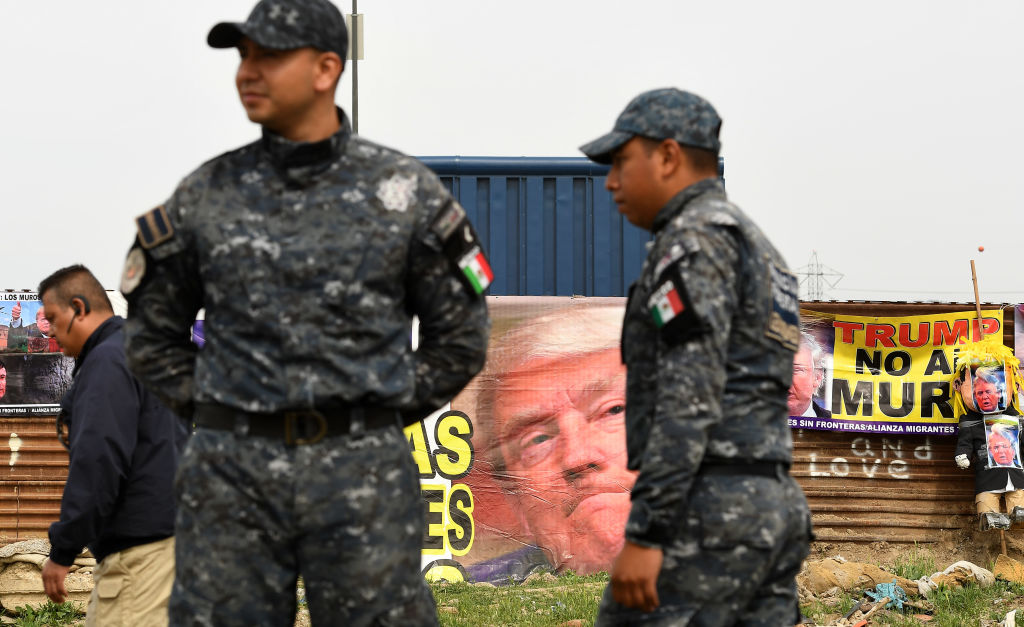 Federal Police stand on the Mexico border side with anti-Trump banners as U.S. police stand guard next to the prototypes of the proposed border wall before President Trump's arrival Tuesday on March 13, 2018 in Tijuana, Mexico. (CREDIT: Wally Skalij/Los Angeles Times via Getty Images)
