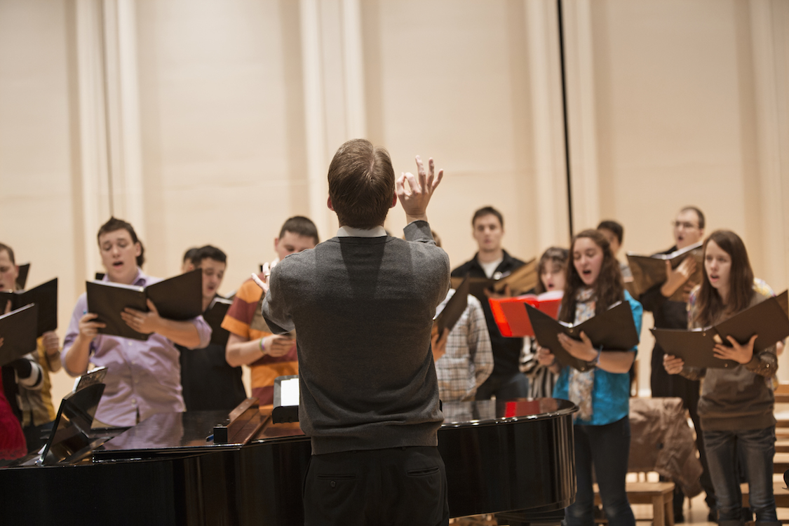 Conductor directing choir on stage. (CREDIT: Getty Images)