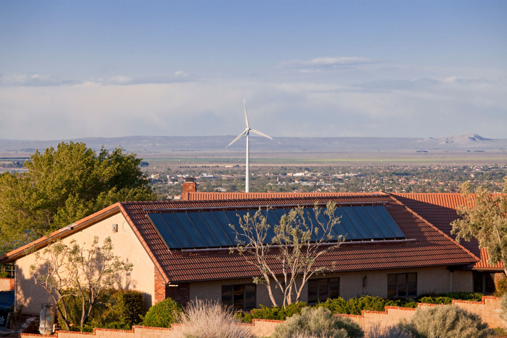 Solar panel on roof with wind turbine nearby in California. CREDIT: Citizens of the Planet/Education Images/UIG via Getty Images