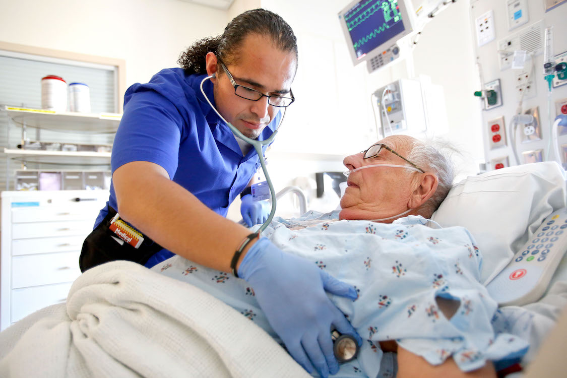 David Fuentes, 25, a student in the masters entry clinical nurse program at UCLA, examines Russell Sherman, 87, a patient. CREDIT: Mel Melcon/Los Angeles Times via Getty Images