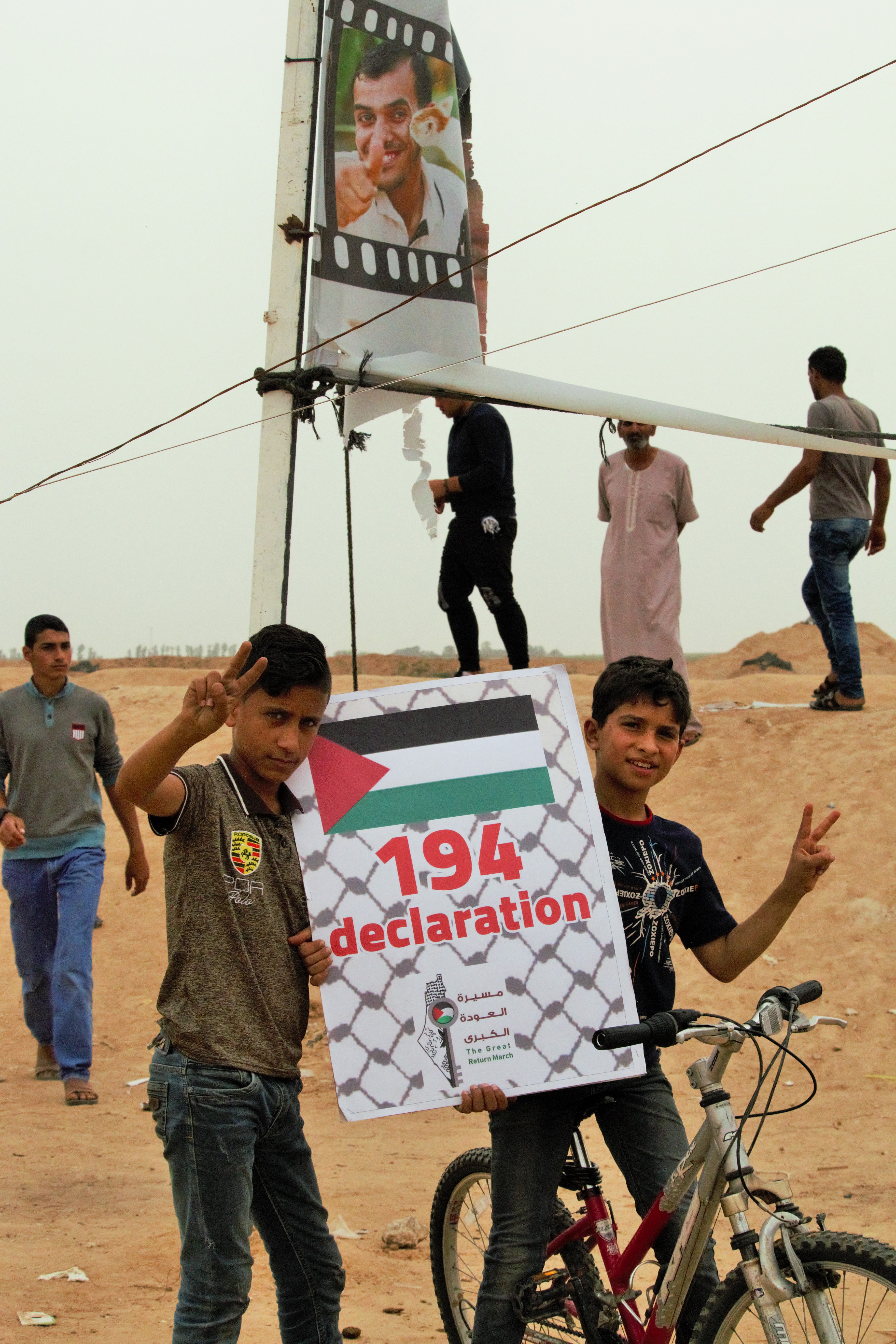 Two boys hold a sign calling for U.N. Resolution 194. A picture of Palestinian journalist Yasser Murtaja, killed on April 6, 2018, is in the background. (Photo courtesy of Intimaa Alsdudi)