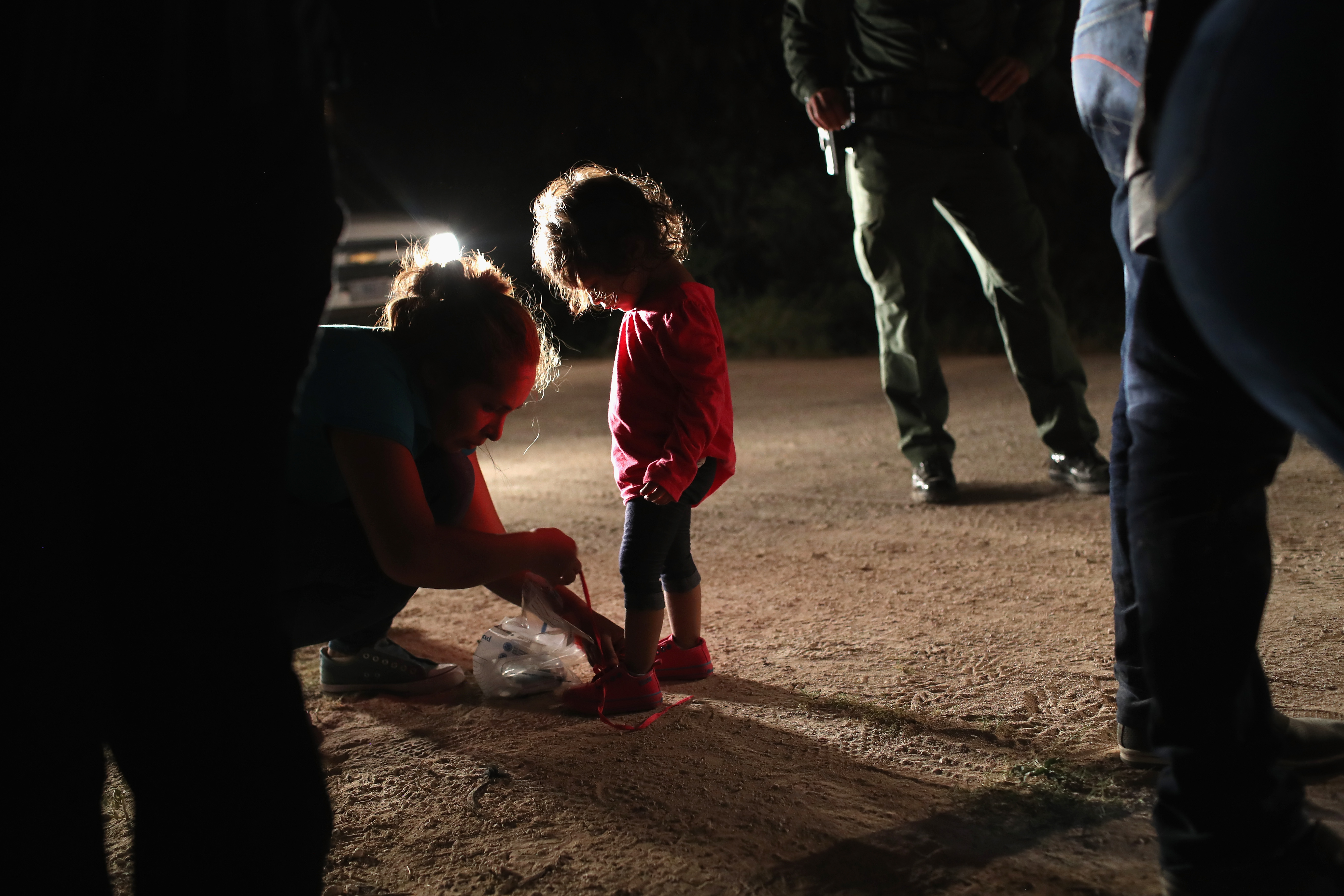 A Honduran mother removes her two-year-old daughter's shoe laces, as required by U.S. Border Patrol agents, after being detained near the U.S.-Mexico border on June 12, 2018 in McAllen, Texas. CRDIT: Photo by John Moore/Getty Images