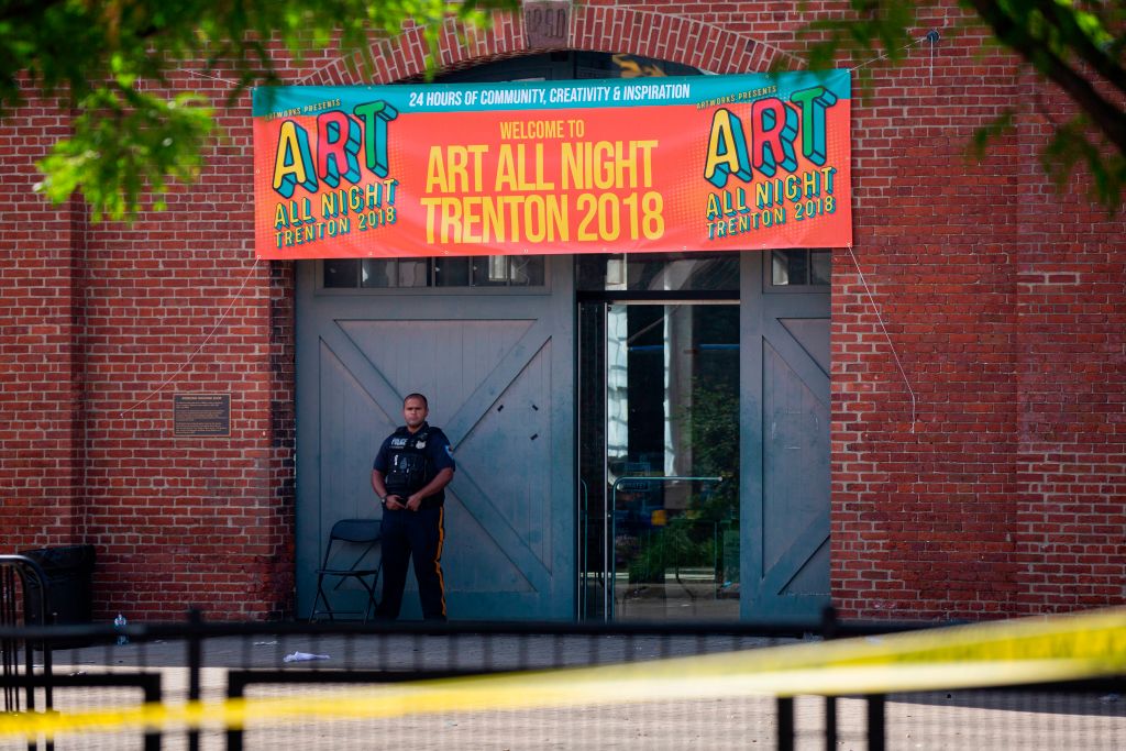 A Police officer stands in front as other officers inspect the crime scene at the Roebling Market on June 17, 2018, the morning after a shooting at an all-night art festival injured 20 people and left one suspect dead in Trenton, New Jersey. (Photo by DOMINICK REUTER/AFP/Getty Images)