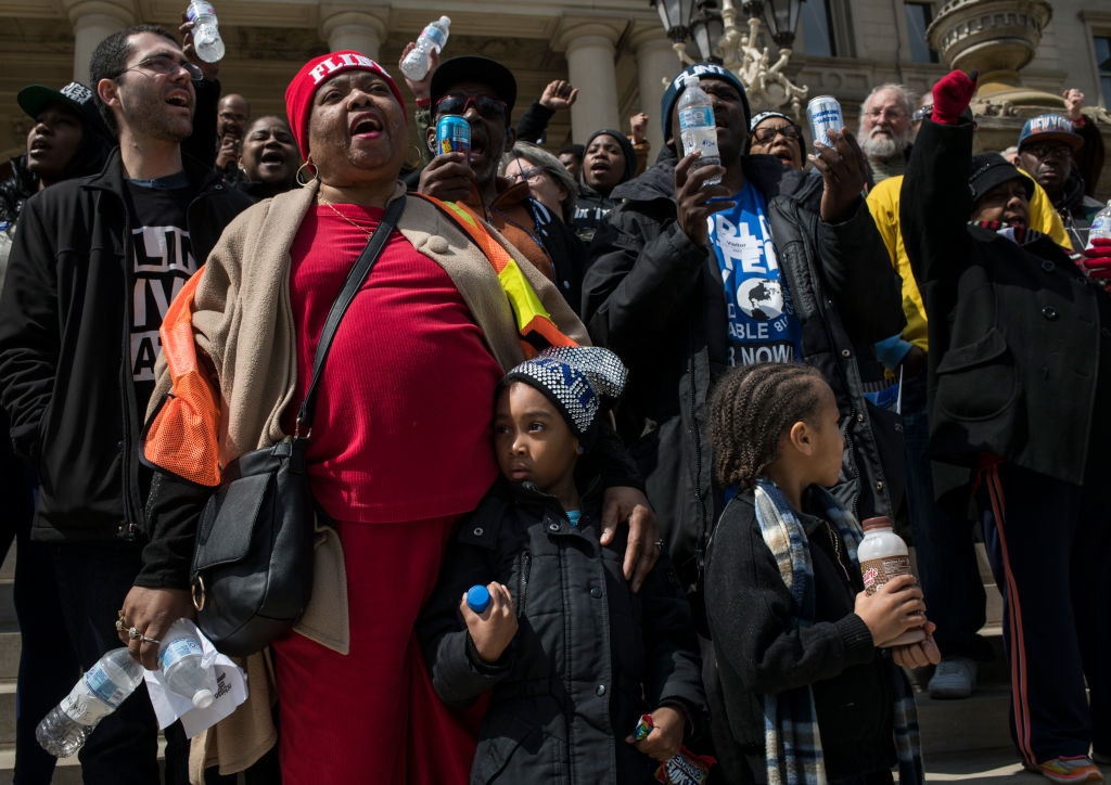 Claudia Perkins, 65, of Flint, Michigan, joins in a chant as her grandchildren, Laila Halford, left, 6, and DeAngelo Perkins, right, 4, watch during a protest on the steps of the Michigan State Capitol on April 11, 2018 in Lansing, Michigan. CREDIT: Brittany Greeson/Getty Images