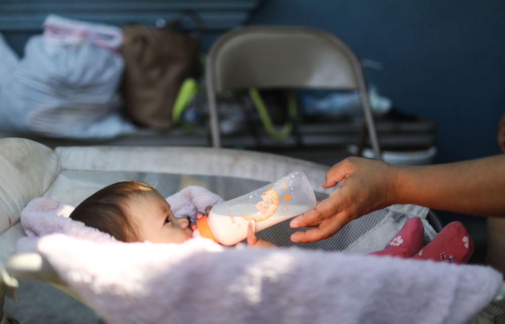 TIJUANA, MEXICO - JUNE 21: A migrant mother feeds a bottle to her daughter in a shelter for migrant women and children on June 21, 2018 in Tijuana, Mexico. The mother, who did not want her name published, said she and her four daughters are seeking asylum in the U.S. after being forced from their home due to death threats. President Trump signed an executive action reversing a decision on the separation of migrant children today. (Photo by Mario Tama/Getty Images)