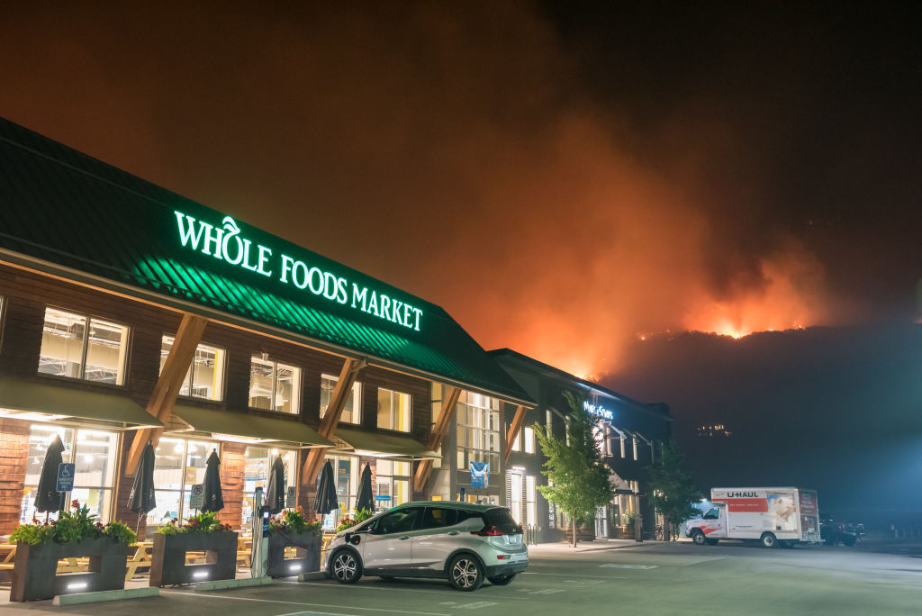 Flames from the Lake Christine fire can be seen rising up across Highway 82 behind Whole Foods in the Willits shopping center late at night on July 4, 2018 in Basalt, Colorado. CREDIT: Chris Council/Getty Images