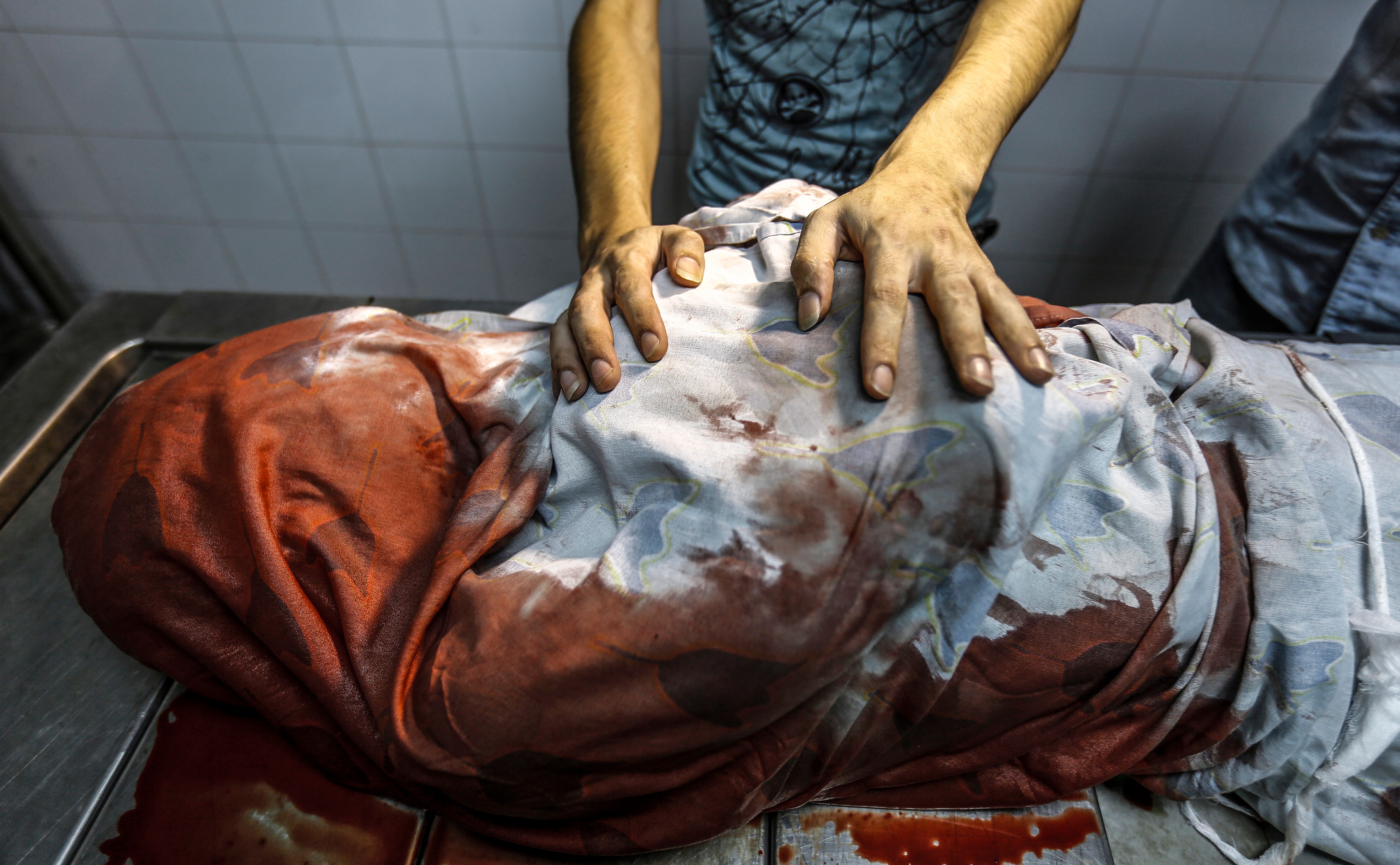 A relative tries to identify the body of a teenage Palestinian who was killed in one of a series of Israeli raids, at al-Shifa hospital morgue in Gaza City on July 14, 2018. CREDIT: Anas Baba/AFP/Getty Images.