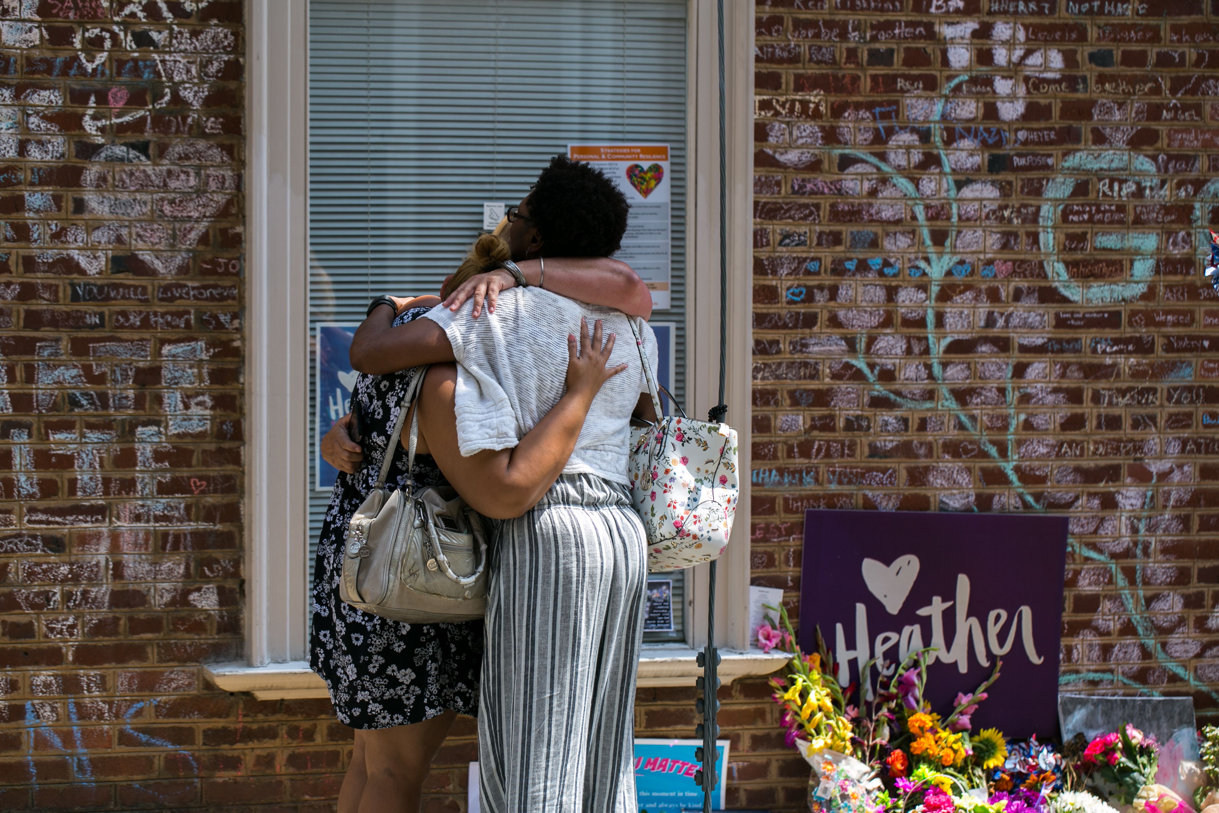 Mourners embrace in front of the hand-written chalk messages that line the walls outside the buildings where one year ago Heather Heyer was killed by a speeding vehicle driven by a white supremacist as she was protesting the Unite The Right rally in Charlottesville, Virginia. CREDIT: Logan Cyrus/AFP/Getty Images)