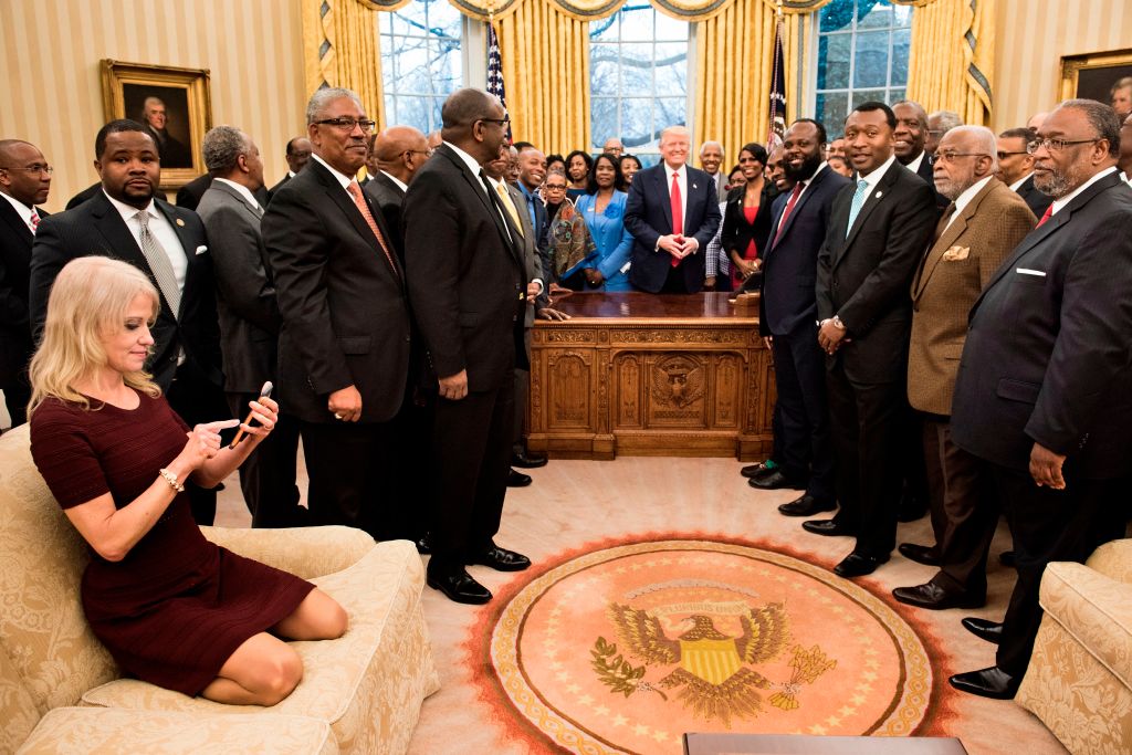 TOPSHOT - Counselor to the President Kellyanne Conway (L) checks her phone after taking a photo as US President Donald Trump and leaders of historically black universities and colleges pose for a group photo in the Oval Office of the White House before a meeting with US Vice President Mike Pence February 27, 2017 in Washington, DC. / AFP PHOTO / Brendan Smialowski (Photo credit should read BRENDAN SMIALOWSKI/AFP/Getty Images)