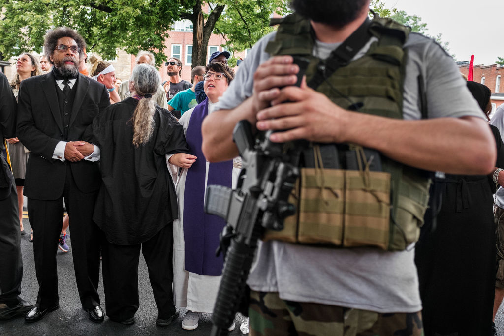 CHARLOTTESVILLE, VIRGINIA - AUGUST 12: Dr. Cornel West locks arms with other members of the clergy while a member of the 3% stands guard holding an assault rifle at the Unite the Right Rally at Emancipation Park on August 12, 2017 in Charlottesville, Virginia. (Photo by Jason Andrew/Getty Images)