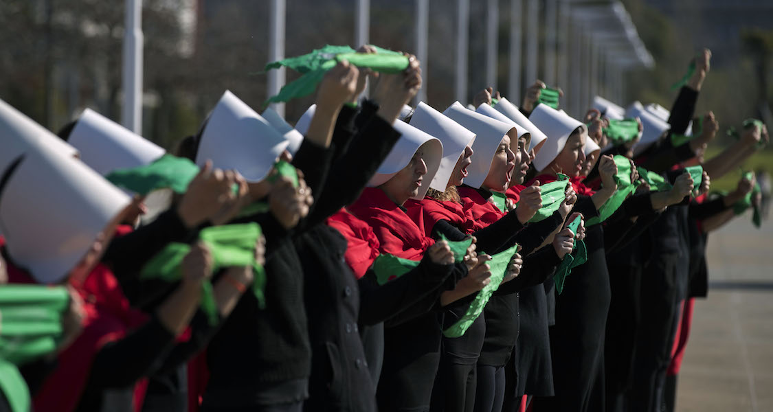 Activists in favor of the legalization of abortion disguised as characters from Canadian author Margaret Atwood's feminist dystopian novel "The Handmaid's Tale", display green headscarves as they perform at the "Parque de la Memoria" in Buenos Aires, on August 5, 2018. (PHOTO CREDIT: Alejandro Pagni /Getty Images)