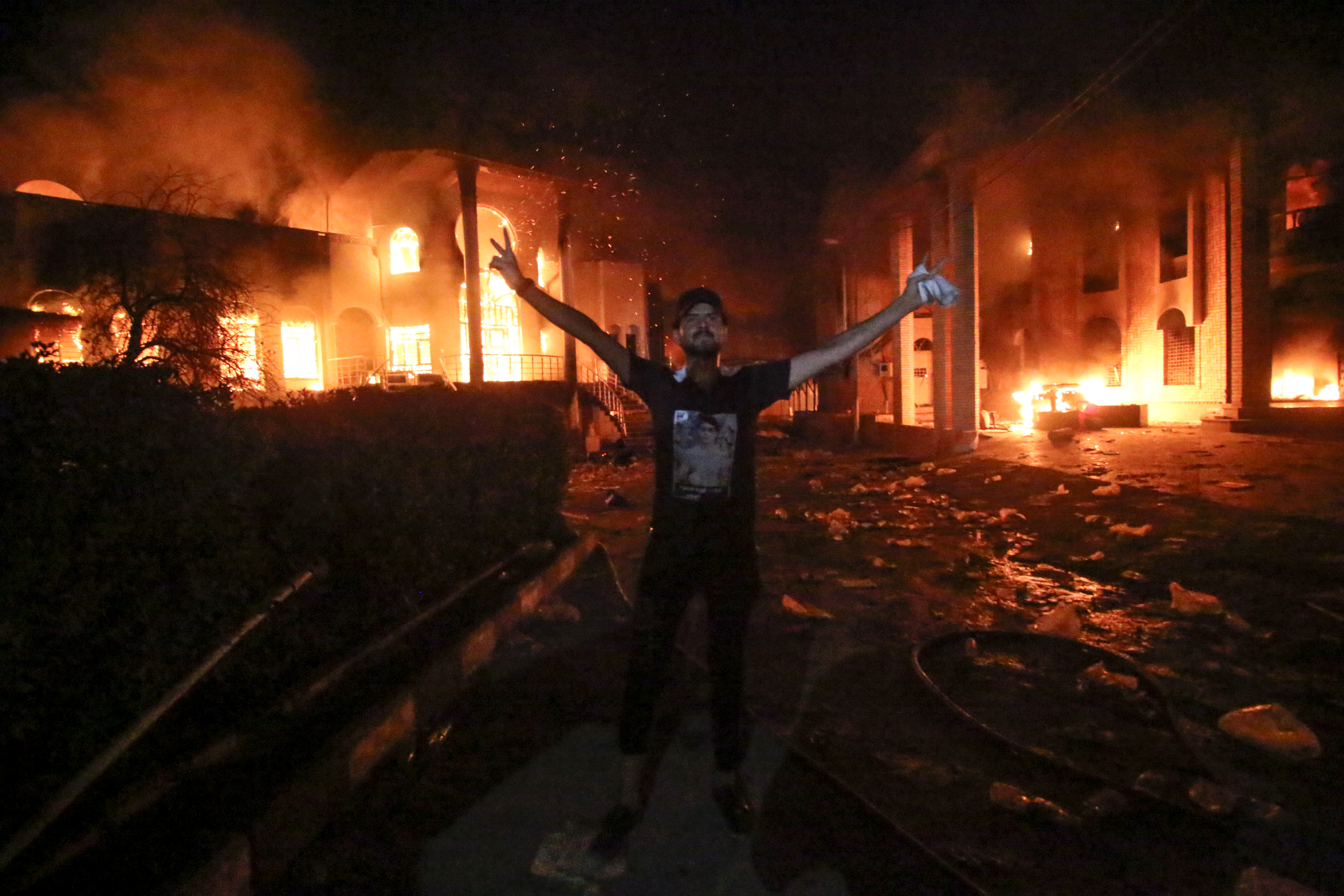 An Iraqi protester stands flashing the victory gesture outside the burning headquarters of the Iranian consulate in the southern city of Basra on September 7, 2018. CREDIT: Haider Mohammed Ali/AFP/Getty Images.