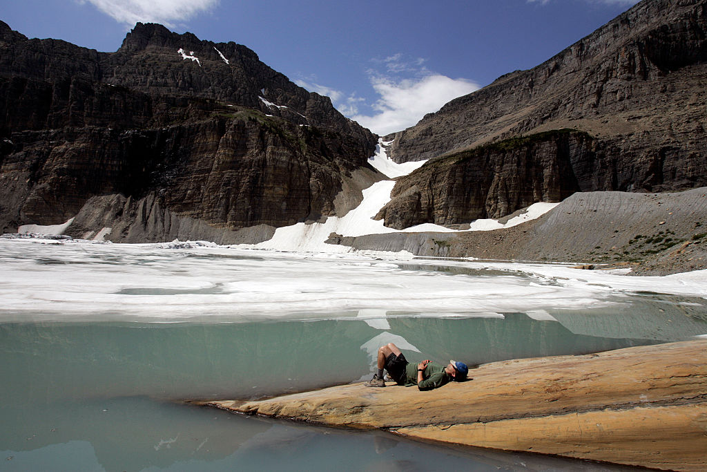 A hiker rests at the edge of the Grinnell Glacier after reaching the top of the Grinnell Glacier Trail at Glacier National Park in Montana. (Credit: Allen J. Schaben/Los Angeles Times via Getty Images)