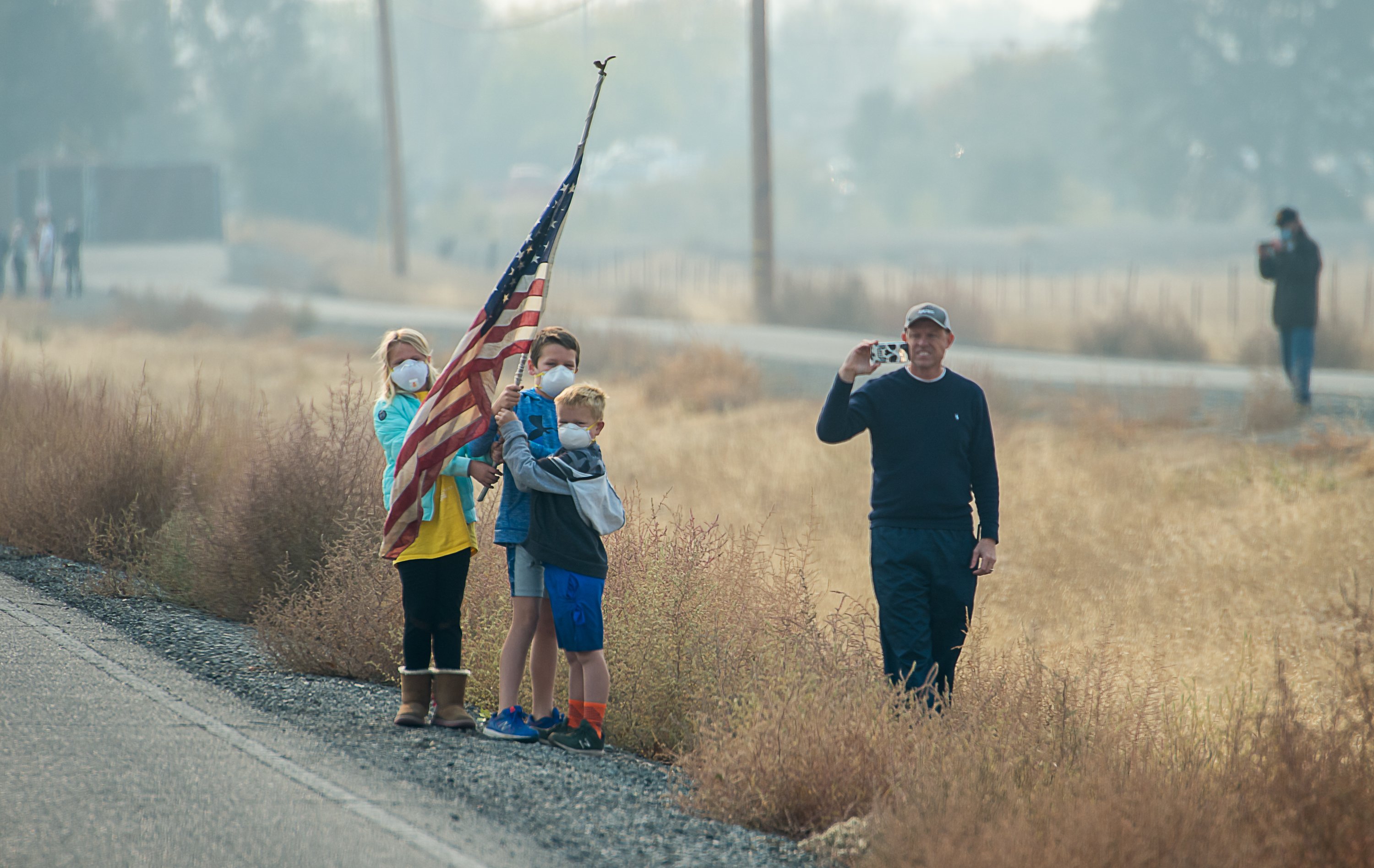 Residents wear masks as they watch the motorcade pass during President Donald Trump visit of the devastating Camp Fire in Chico, California on November 17, 2018. The National Climate Assessment, released last week, revealed a number of troubling predictions, including an increase in both the number and intensity of such wildfires. (Photo Credit: Paul Kitagaki Jr.-Pool/Getty Images)