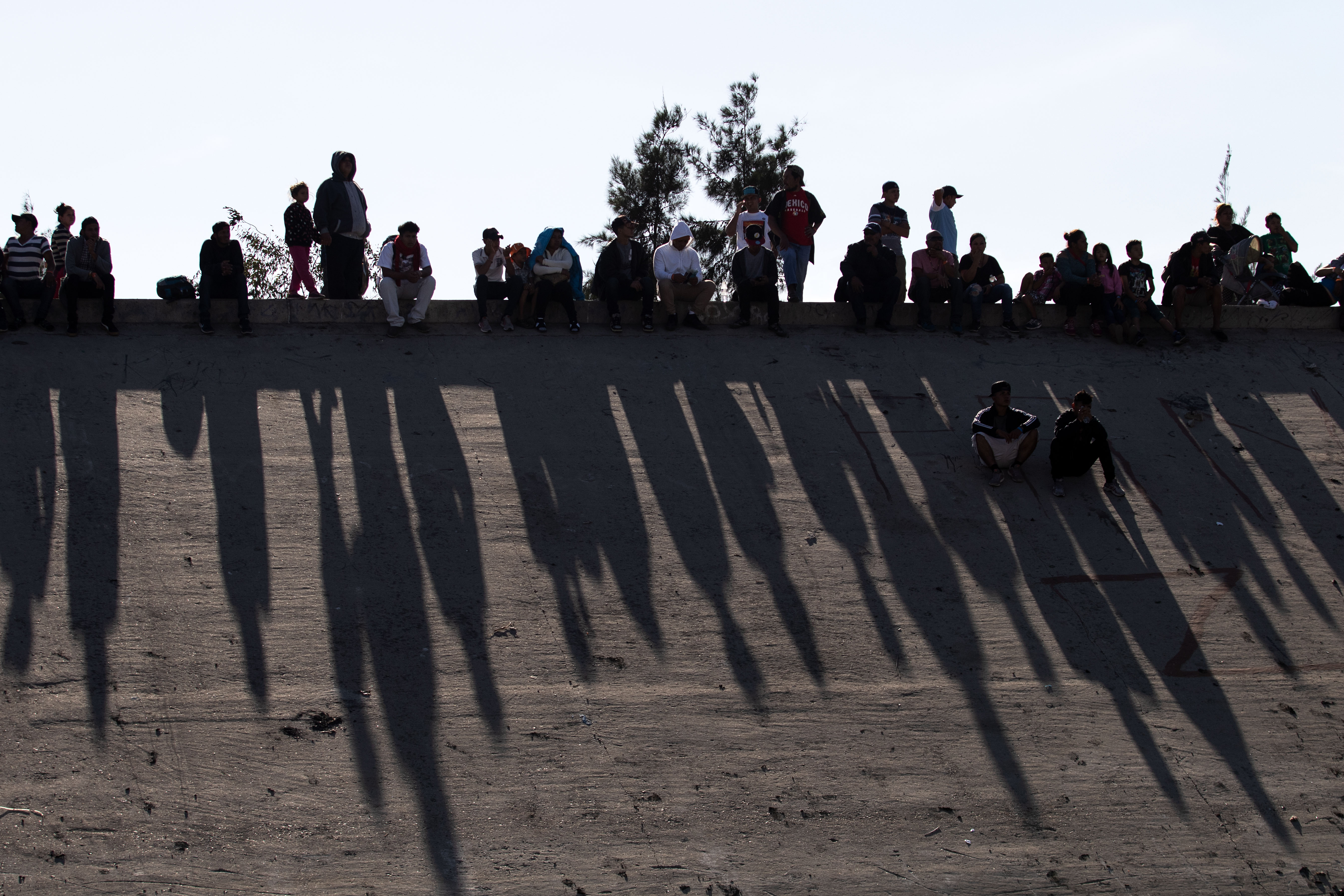 Central American migrants -mostly from Honduras - sit along the concrete waterway of the bordering Tijuana River right across the El Chaparral border crossing point in Tijuana, Baja California State, Mexico, on November 25, 2018. US officials closed the San Ysidro crossing point in southern California on Sunday after hundreds of migrants tried to enter the country. (Photo credit: GUILLERMO ARIAS/AFP/Getty Images)