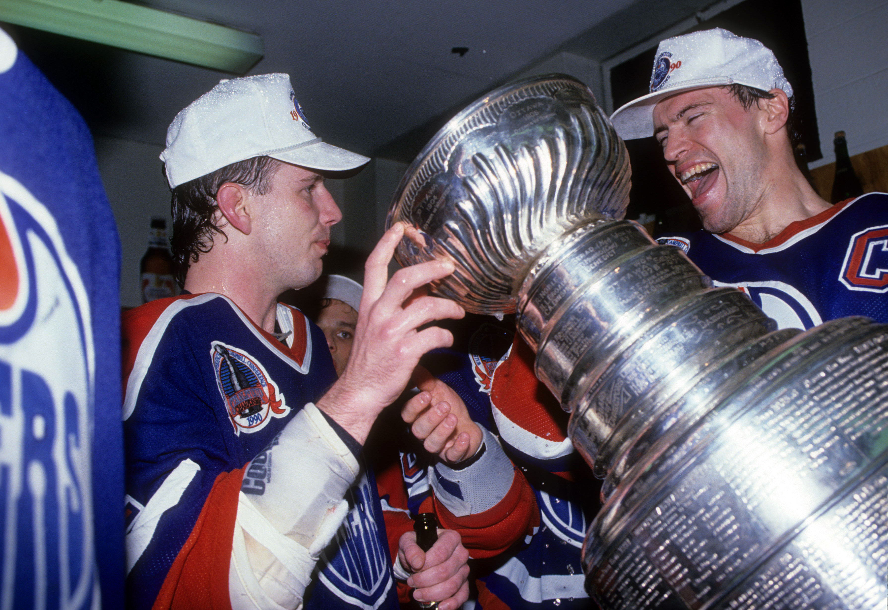 BOSTON, MA - MAY 24: Mark Messier #11 of the Edmonton Oilers helps out teammate Joe Murphy drink from the Stanley Cup in the locker room as they celebrate after Game 5 of the 1990 Stanley Cup Finals against the Boston Bruins on May 24, 1990 at the Boston Garden in Boston, Massachusetts. The Oilers defeated the Bruins 4-1 and won the Series 4 games to 1. (Photo by B Bennett/Getty Images)