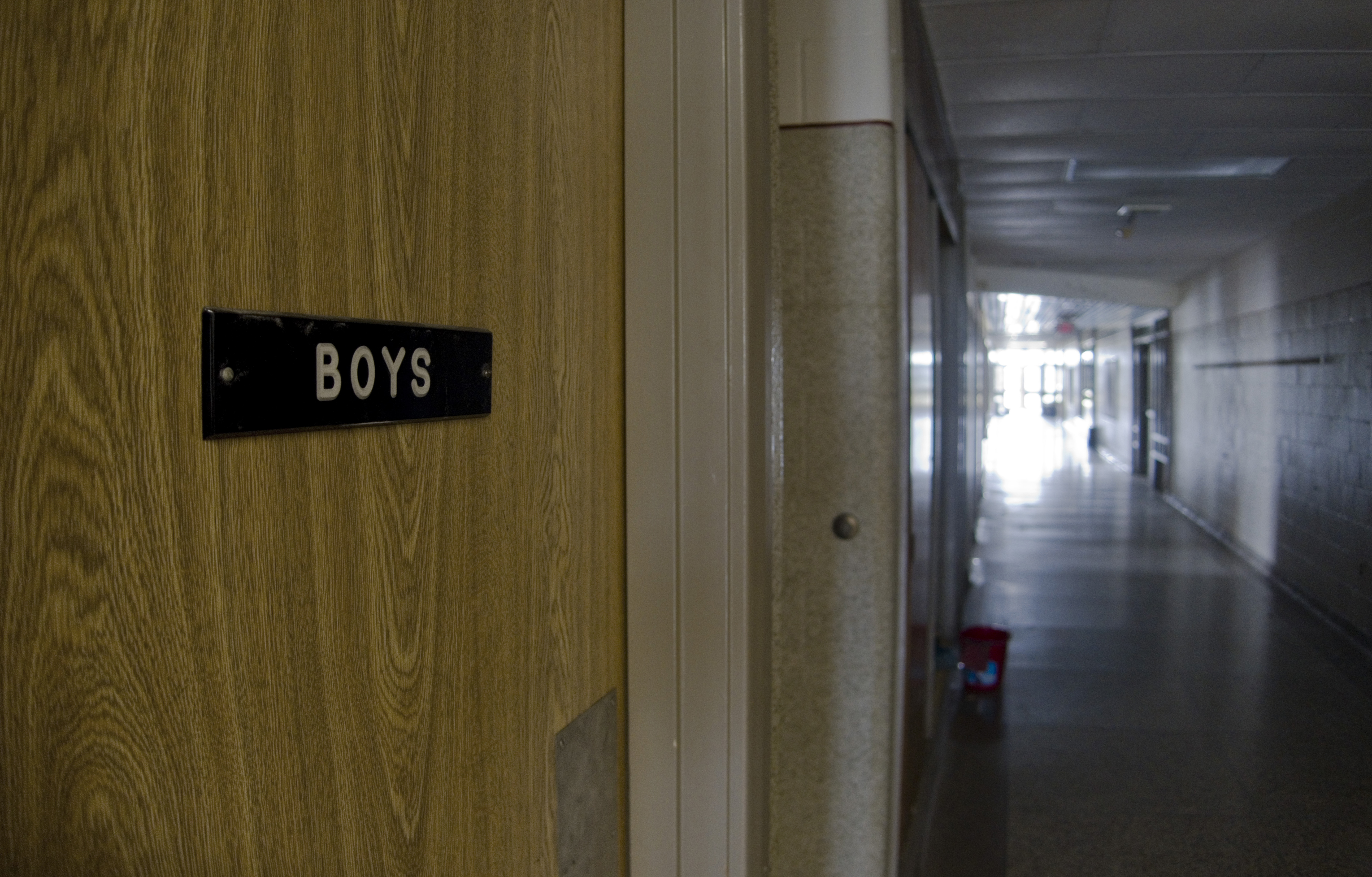 Sign on boys room door in a dark school hall.