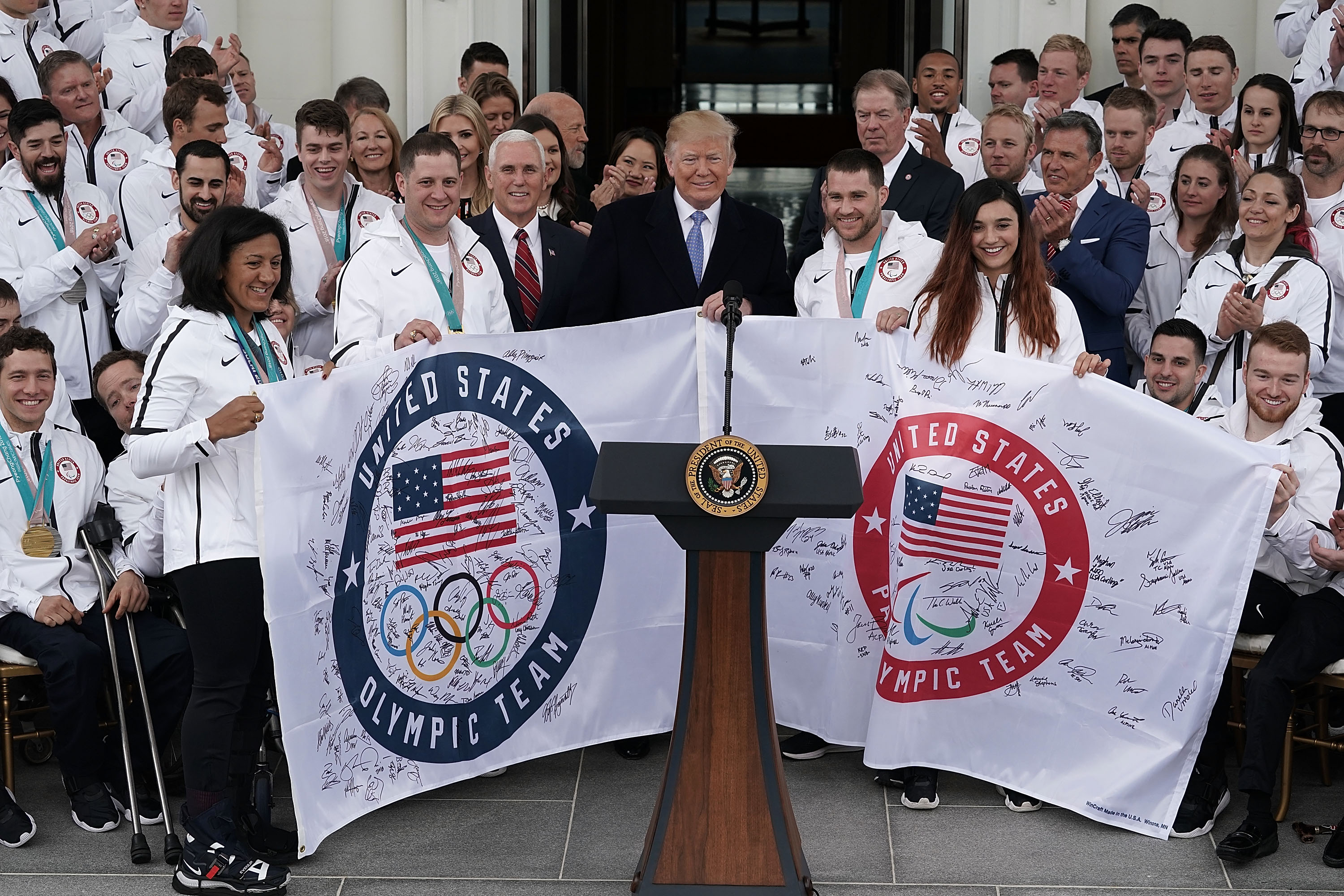 WASHINGTON, DC - APRIL 27: U.S. President Donald Trump is presented with two flags as he hosts Team USA at the North Portico of the White House April 27, 2018 in Washington, DC. President Trump hosted the team to celebrate their victories in the 2018 Winter Olympics. Holding the Olympic Team flag are bobsledder Elana Meyers Taylor and curler John Shuster. Holding the Paralympic Team flag are snowboarder Mike Schultz and snowboarder Brenna Huckaby. (Photo by Alex Wong/Getty Images)